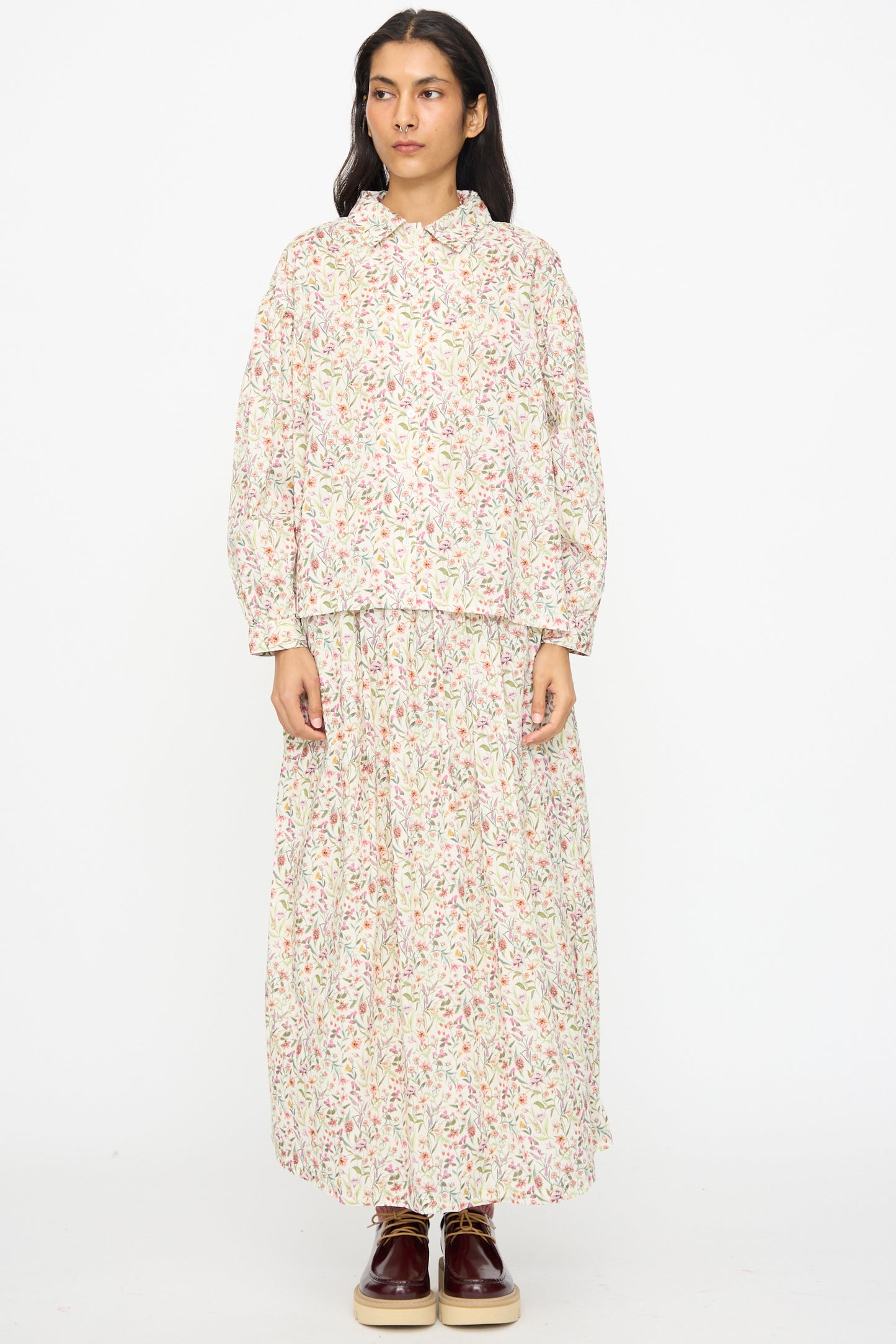 A person wearing the Ichi Antiquités Cotton Liberty Shirt in Flower Print with a matching long skirt and brown shoes stands against a plain white background.