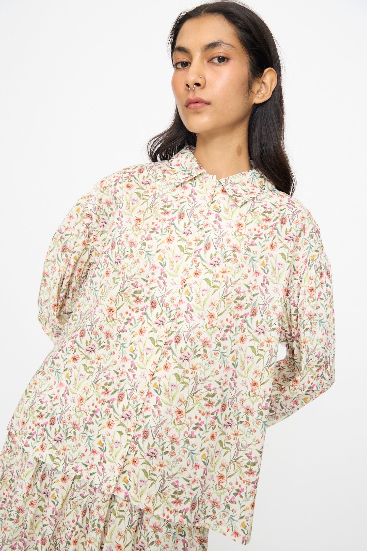A woman with long dark hair wears the Ichi Antiquités Cotton Liberty Shirt in Flower Print, a loose-fitting, collared floral top in pastel tones, standing against a plain white background.