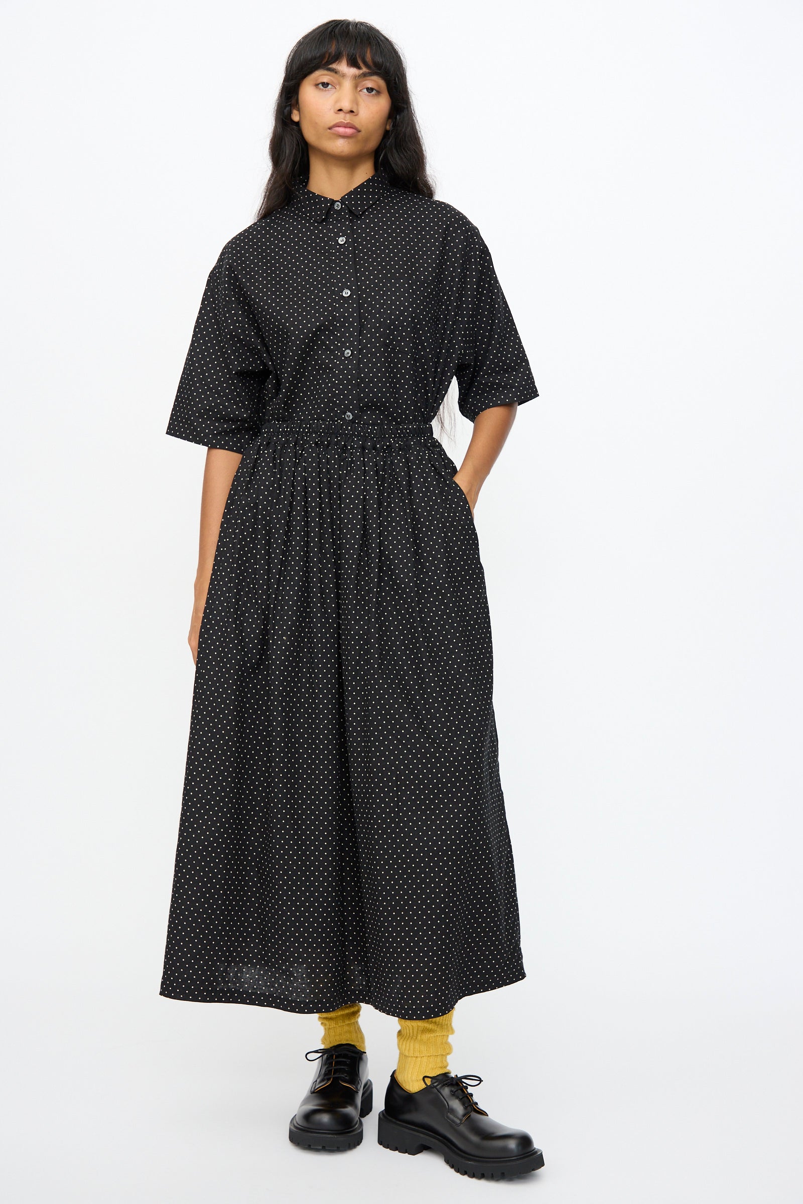 A person wears the Ichi Antiquités Cotton Linen Dot Skirt in Black, paired with black shoes and yellow socks, standing against a plain white background.