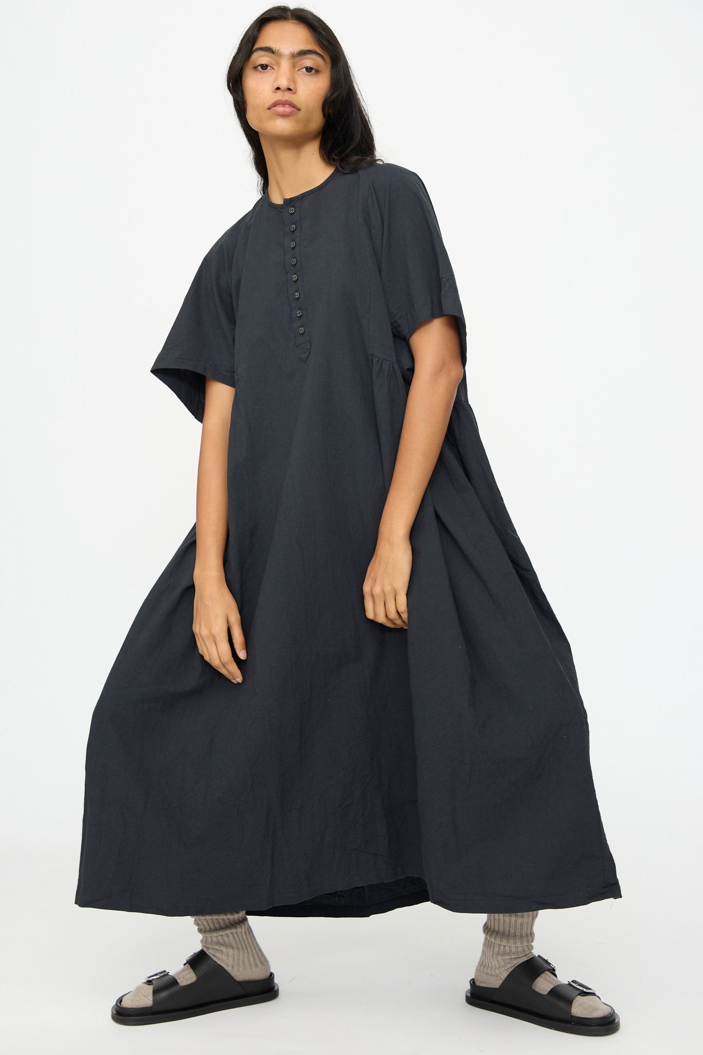 A person wearing the Ichi Antiquités Cotton Linen Dress in Black with black sandals and beige socks, standing against a plain white background.