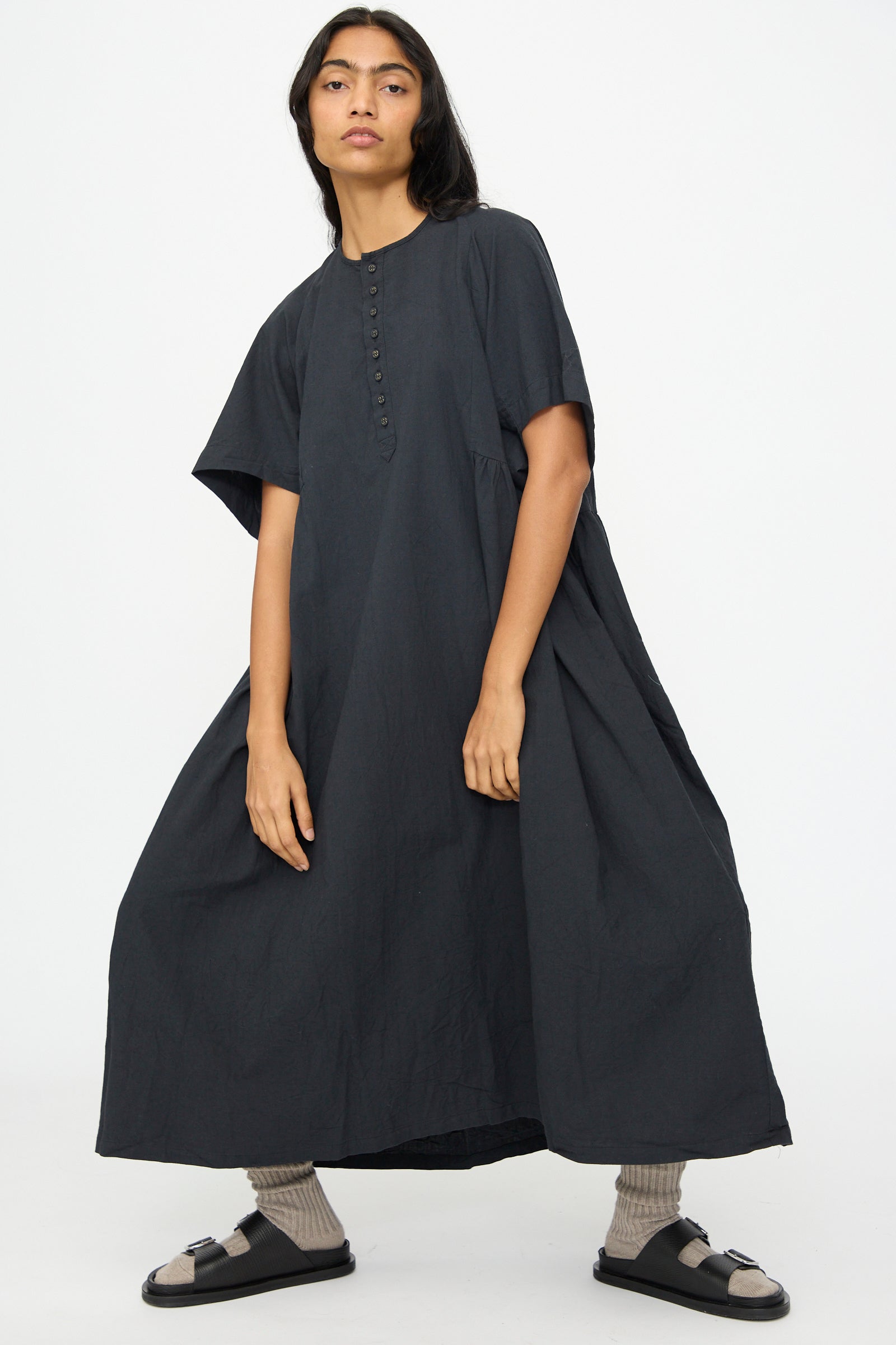 A person wearing the Ichi Antiquités Cotton Linen Dress in Black with black sandals and beige socks, standing against a plain white background.