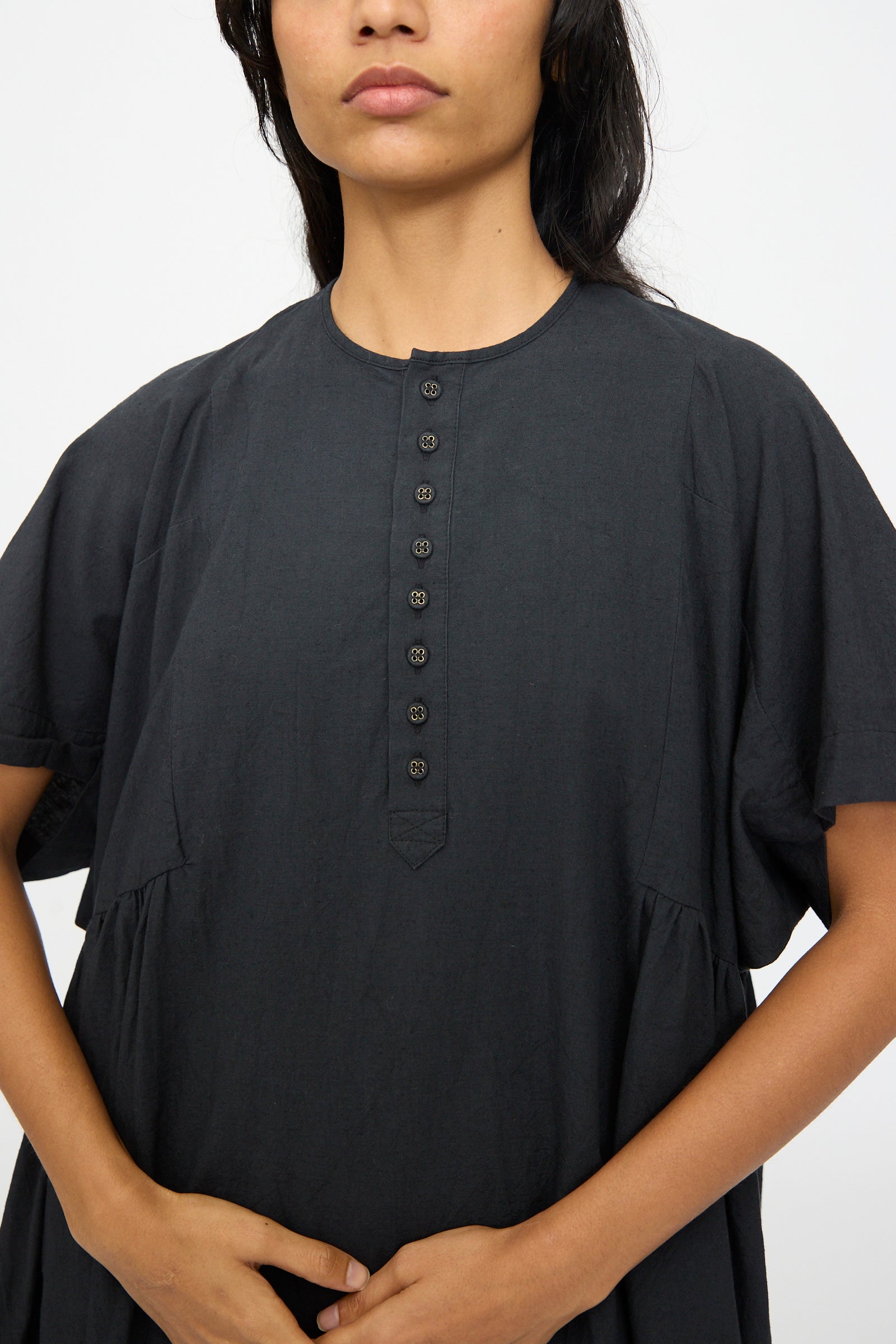 A person wears the Ichi Antiquités Cotton Linen Dress in Black, a loose-fitting short-sleeve dress with a round neckline and front buttons. The face is partially visible.