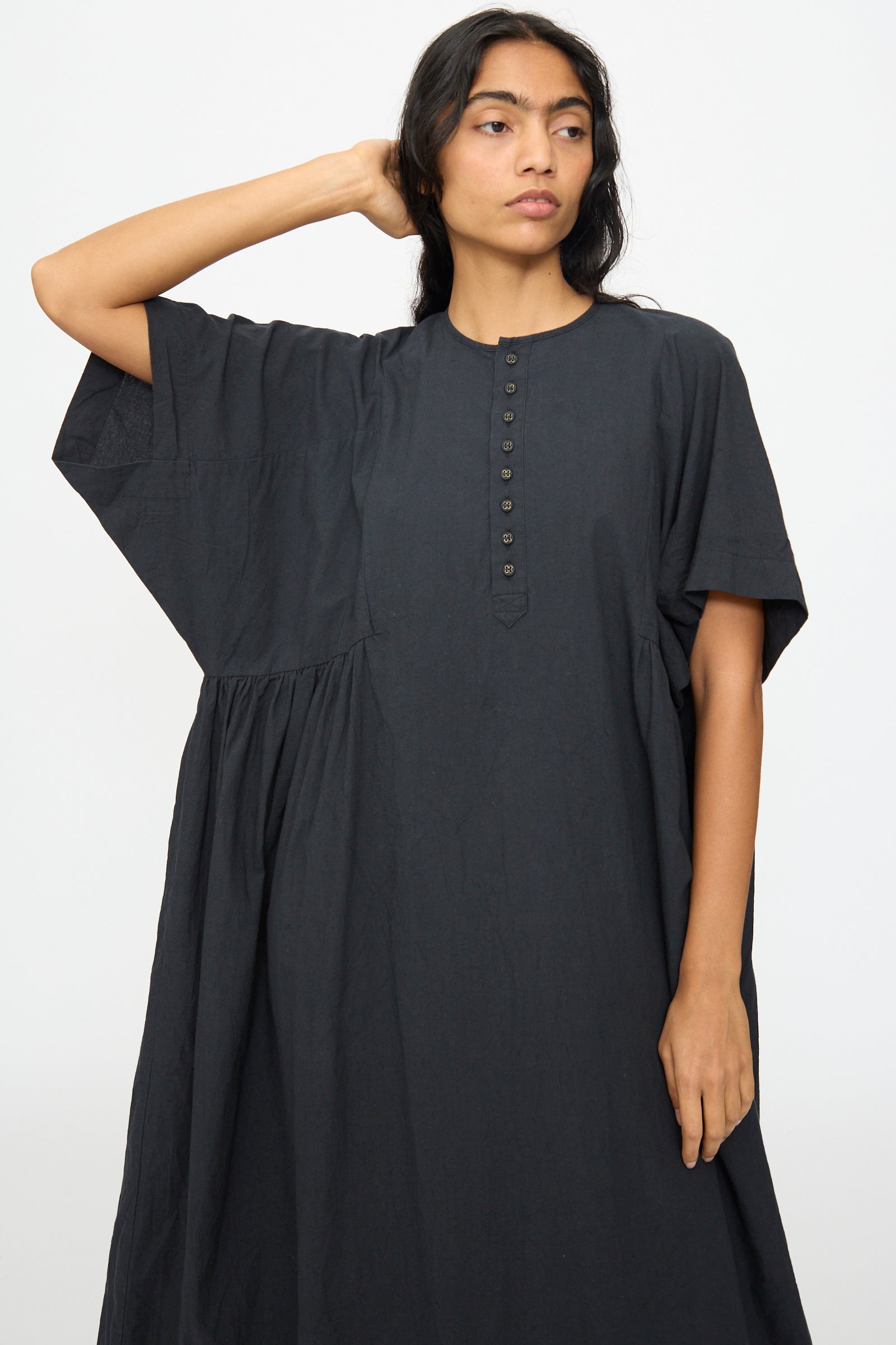 A woman wears the Ichi Antiquités Cotton Linen Dress in Black, featuring an oversized fit and short sleeves with a buttoned front, standing against a plain white background.