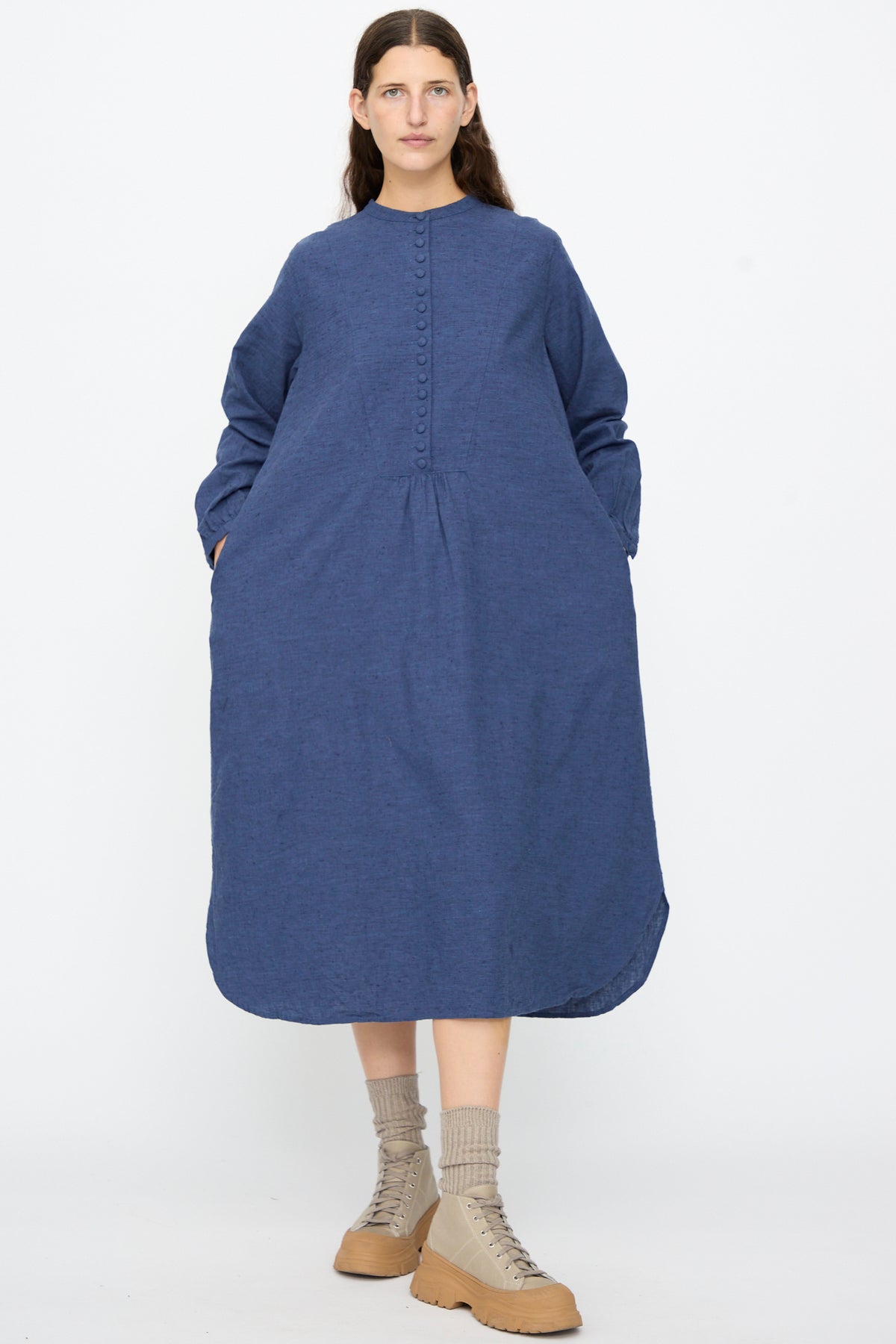 A person wears an Ichi Antiquités Cotton Linen Nep Dress in Navy, a midi-length button-front dress with long sleeves and a rounded hem, paired with beige lace-up boots and mid-calf socks.