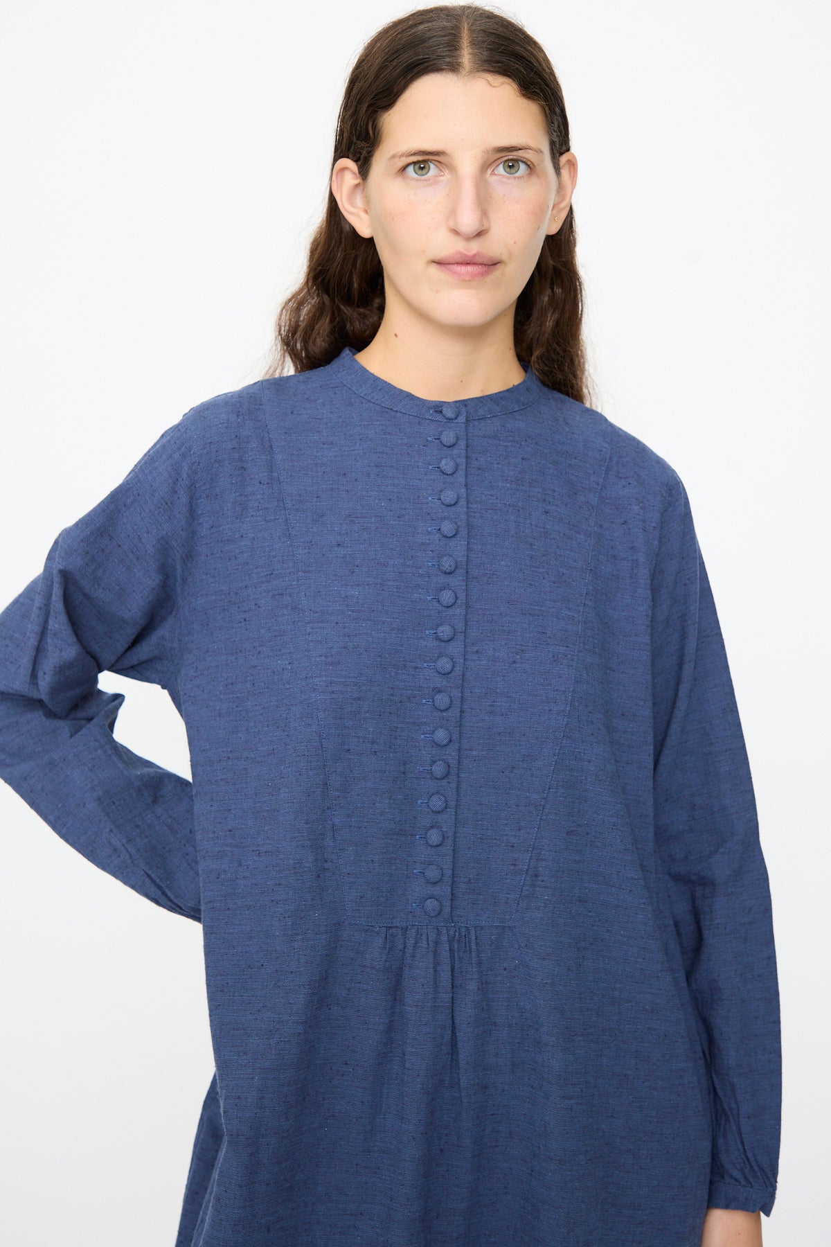 A person wears an Ichi Antiquités Cotton Linen Nep Dress in navy, featuring a long-sleeved silhouette, band collar, and a row of fabric-covered buttons down the front.