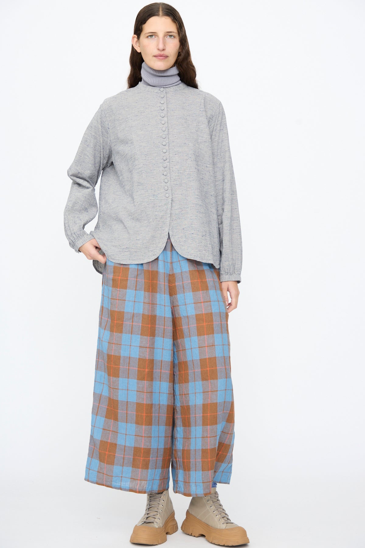A person wearing an Ichi Antiquités Cotton Linen Nep Shirt in Natural over a turtleneck, paired with wide-leg blue and brown plaid trousers and tan lace-up boots.