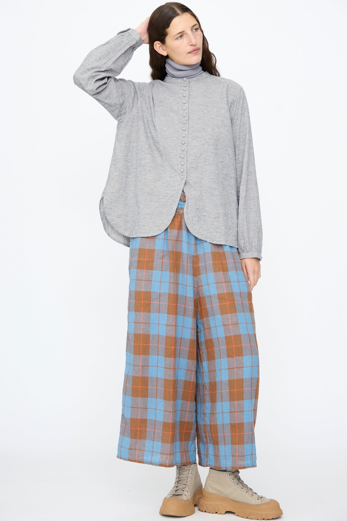 A person wearing an Ichi Antiquités Cotton Linen Nep Shirt in Natural over a grey turtleneck, paired with wide-leg blue and brown plaid trousers and tan lace-up sneakers.