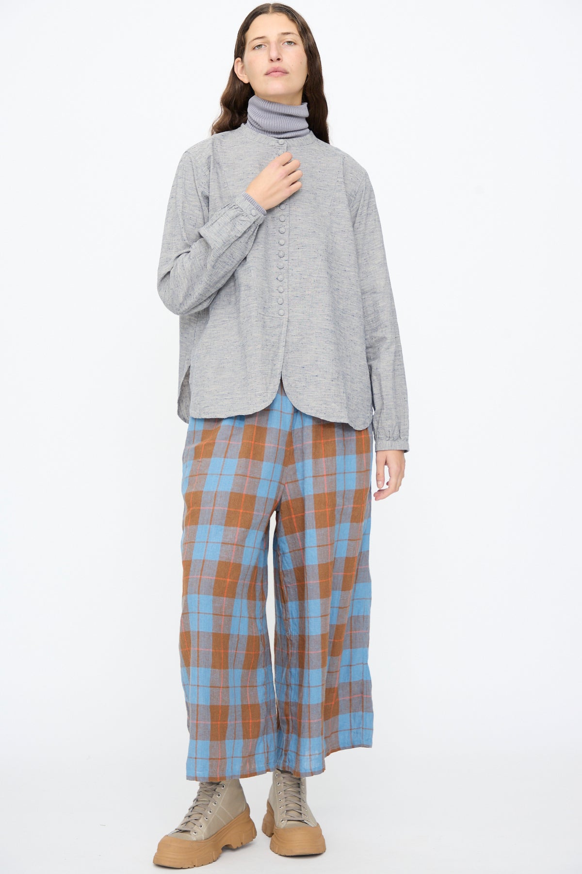 A person wearing an Ichi Antiquités Cotton Linen Nep Shirt in Natural over a grey turtleneck, blue and brown plaid wide-leg trousers, and tan lace-up boots.