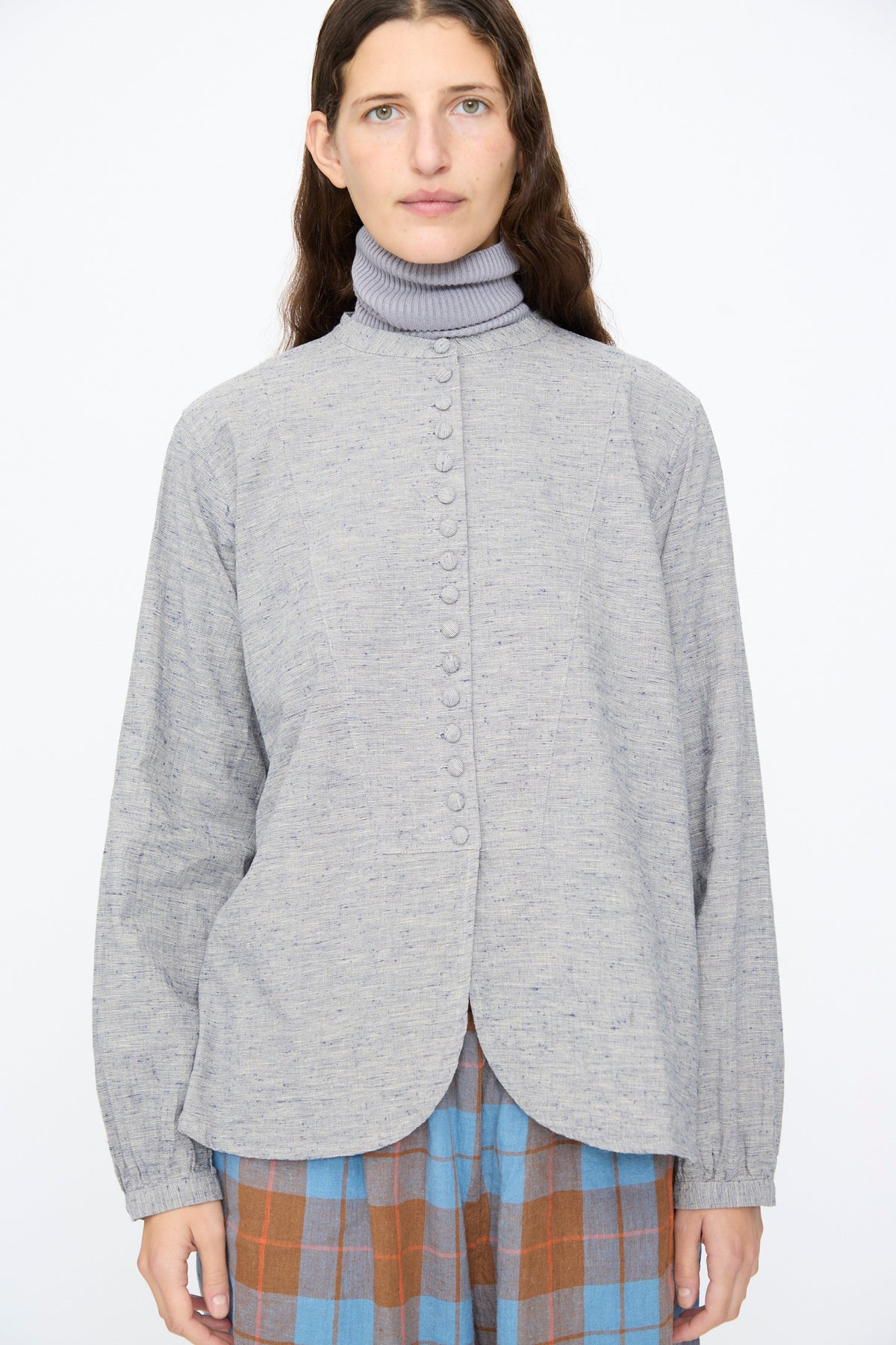 An Ichi Antiquités Cotton Linen Nep Shirt in Natural, featuring a grey band collar, worn over a grey turtleneck and a blue and brown plaid skirt.