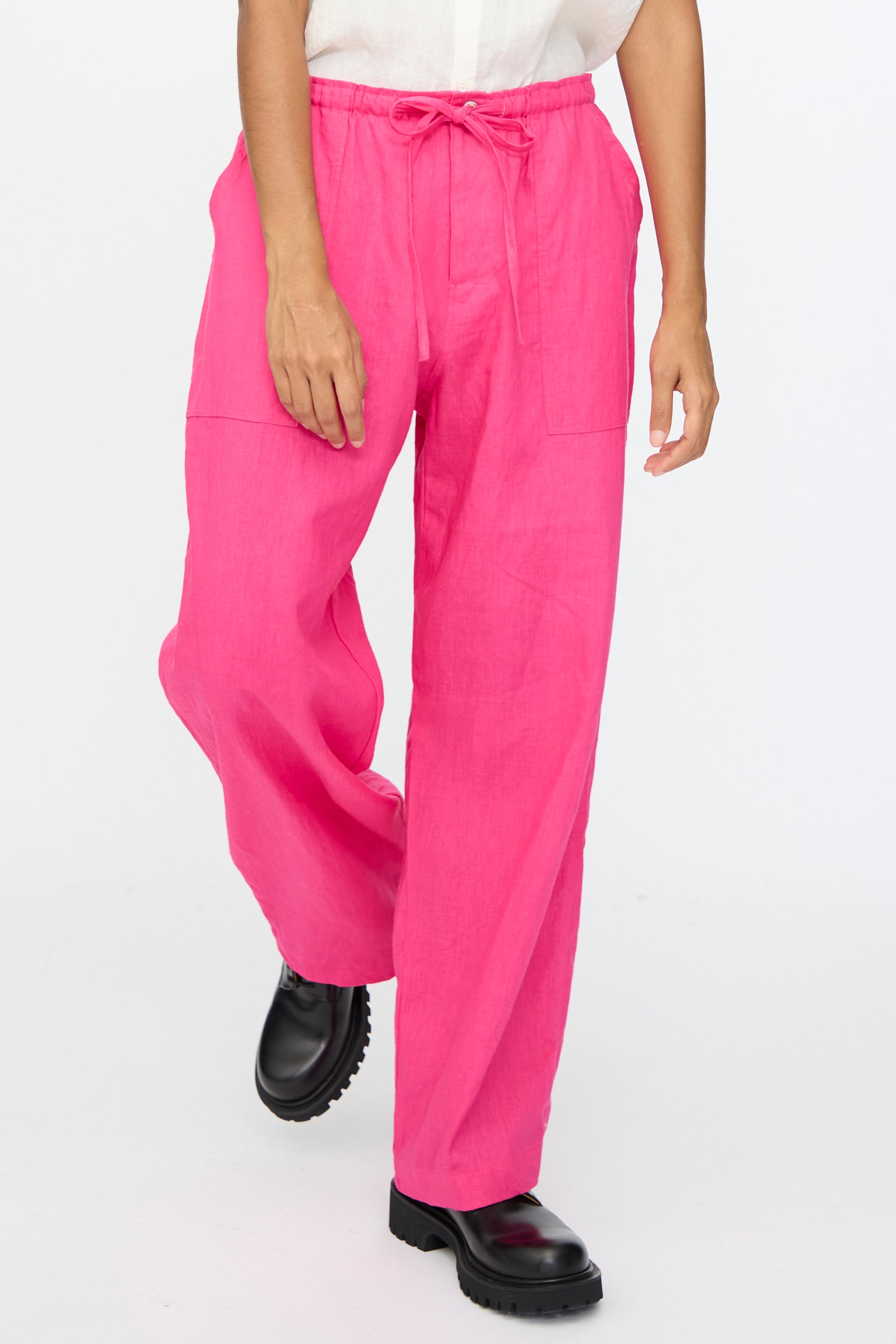 A person wears Ichi Antiquités Color Linen Pants in Pink with a relaxed fit, paired with a white shirt and black shoes, standing against a plain white background.