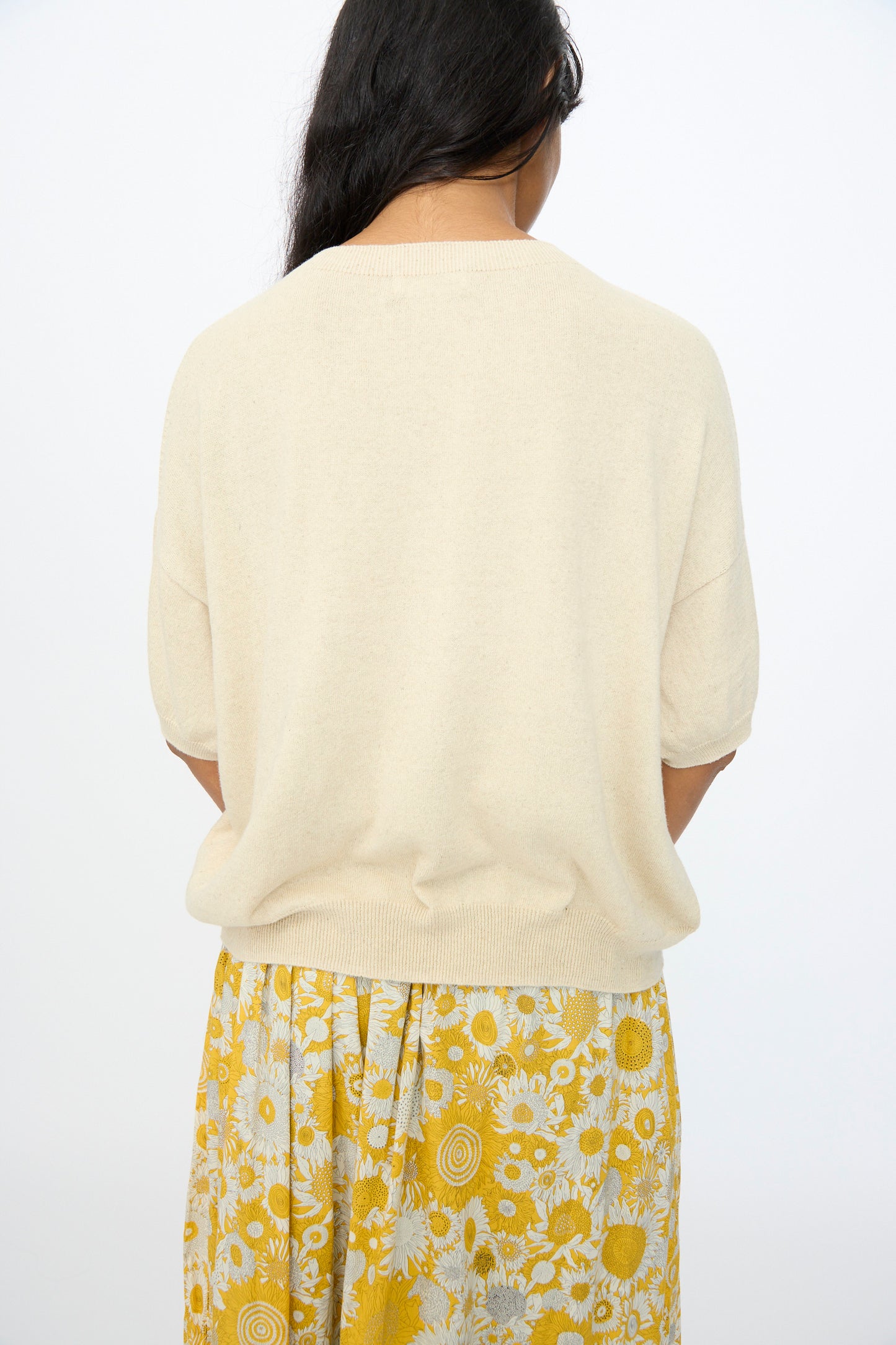 A person with long dark hair, seen from behind, wears the Ichi Antiquités Cotton Linen Pullover in Natural and a yellow skirt with a white floral pattern.
