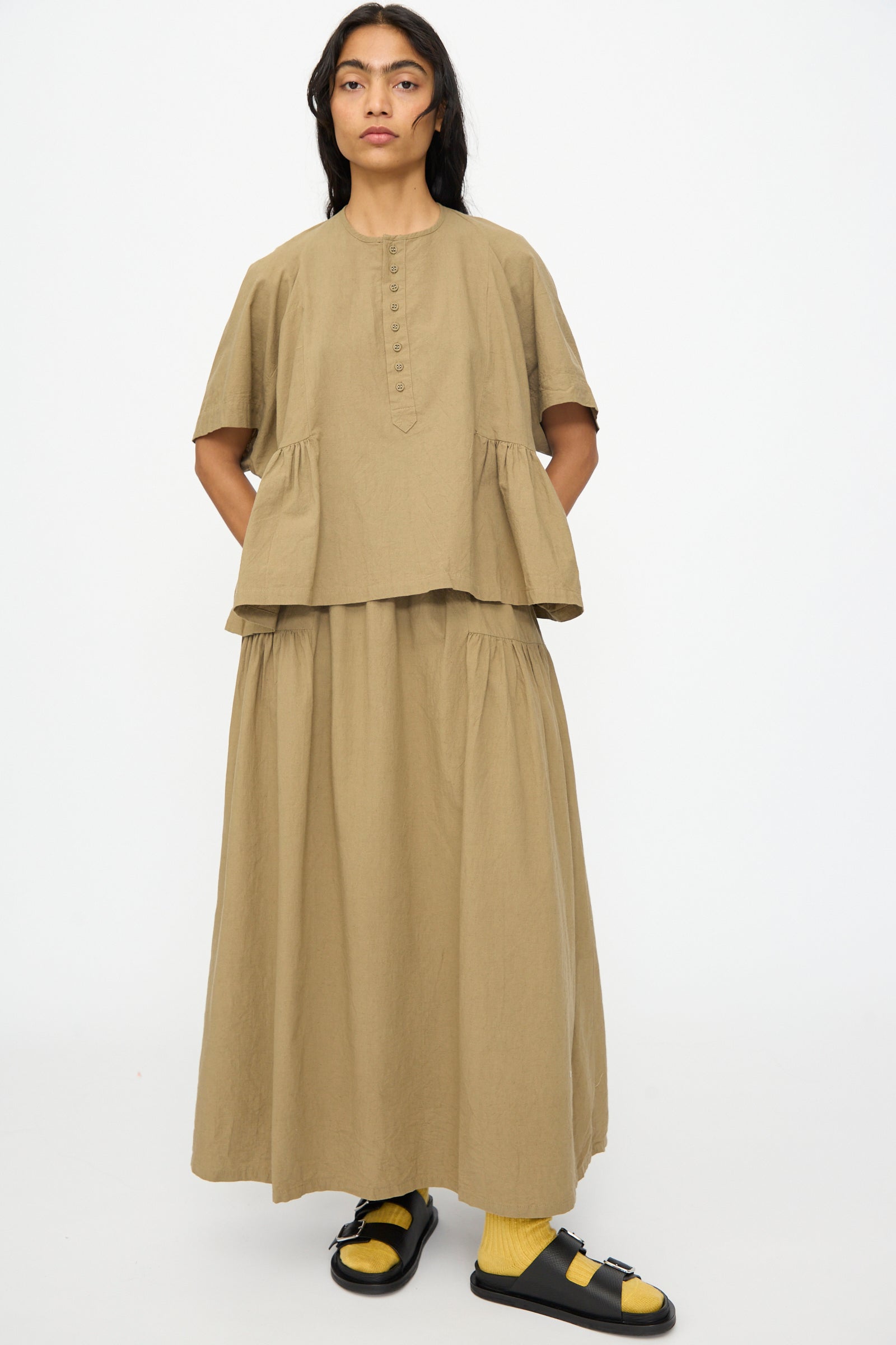 A person stands facing forward wearing the Ichi Antiquités Cotton Linen Shirt in Mocha, styled with a matching long skirt and black sandals with yellow socks.