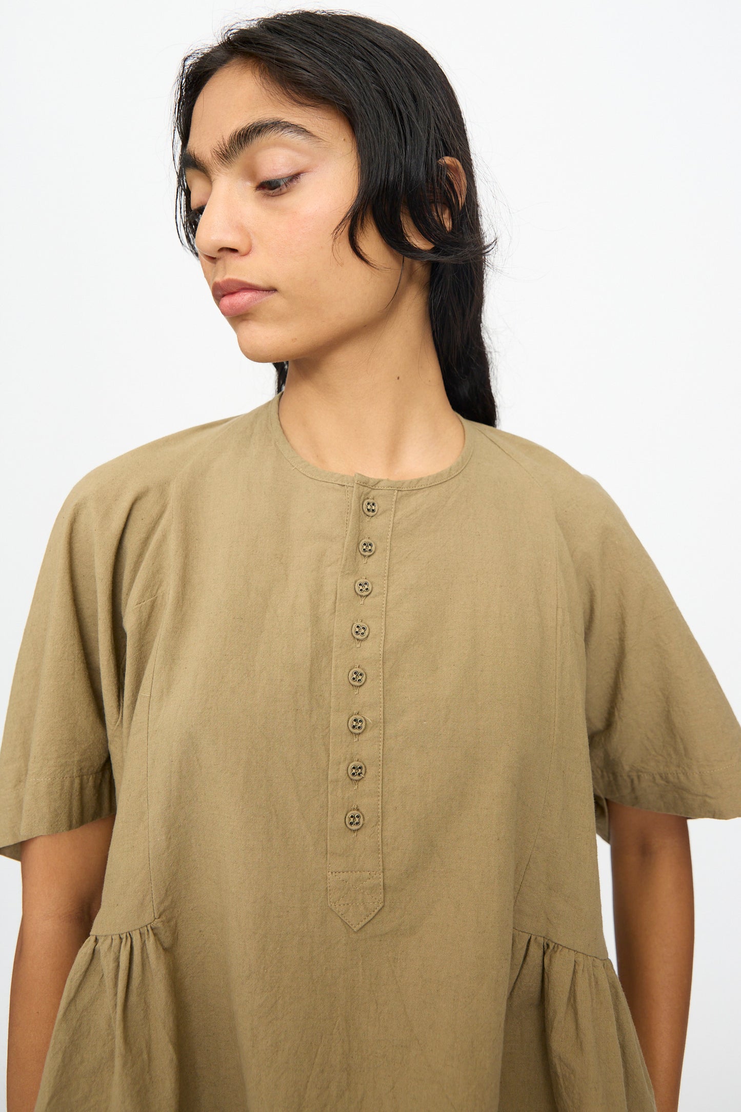A person in the Ichi Antiquités Cotton Linen Shirt in Mocha, a loose-fitting, short-sleeved dress, looks to the side against a plain white background.
