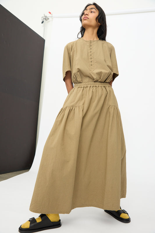 A person stands in a studio wearing the Ichi Antiquités Cotton Linen Skirt in Mocha, styled with yellow socks and black sandals.