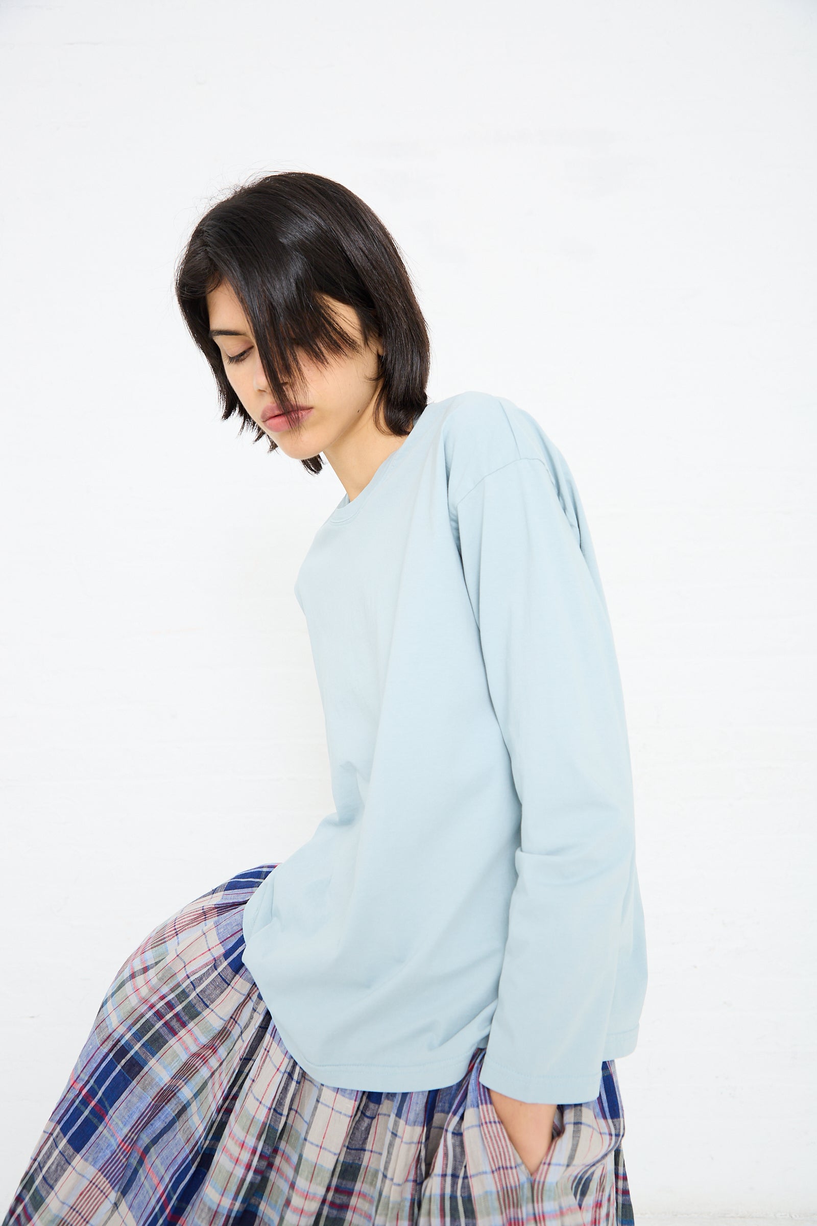 A person with short dark hair is wearing a light blue **Cotton Long Sleeve Pullover Tee in Blue** from **Ichi Antiquités** paired with a plaid skirt.