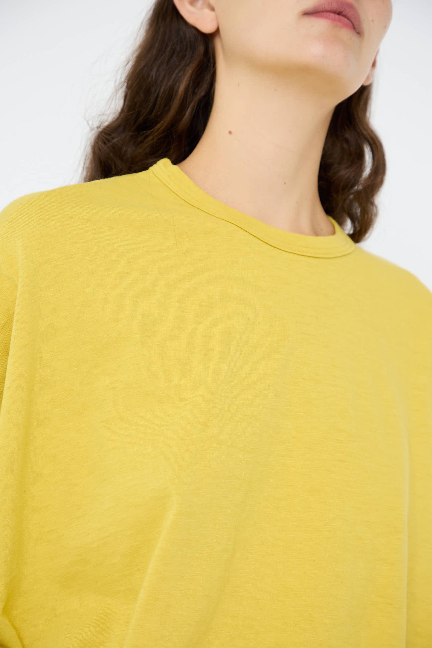 An individual wearing the Cotton Loose Long Sleeve Pullover in Mustard by Ichi Antiquités, with long brown hair cascading over their shoulders, is positioned against a plain background. This casual cotton piece exudes a relaxed vibe, although their head is partially out of frame.