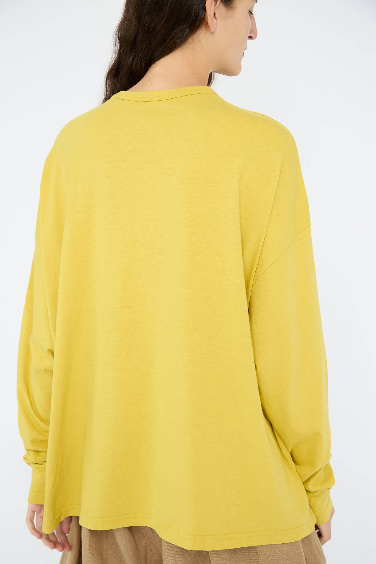 A person wearing the Cotton Loose Long Sleeve Pullover in Mustard from Ichi Antiquités and boxy-fit brown pants is facing away from the camera against a plain background.