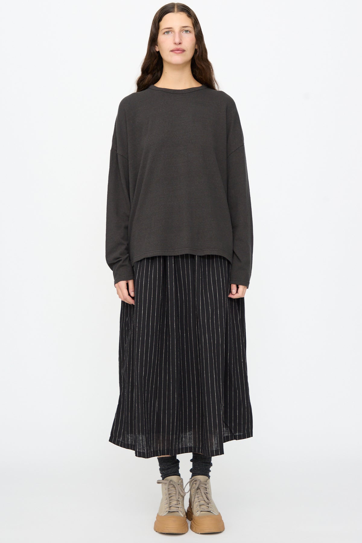 A person wears an Ichi Antiquités Cotton Loose Pullover in Black with a black pinstriped midi skirt, dark socks, and tan lace-up shoes.