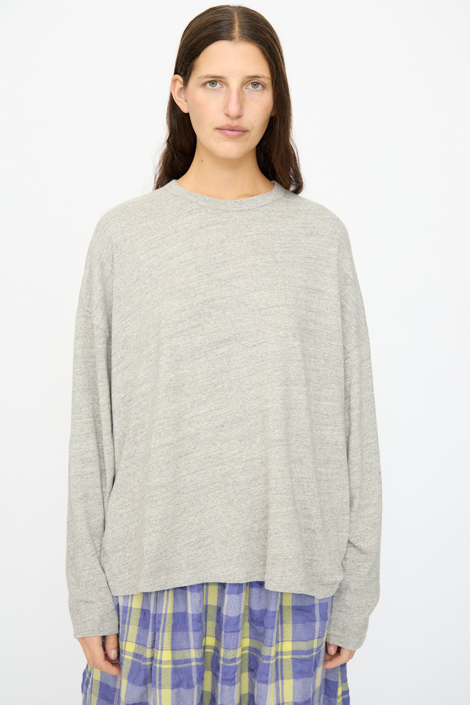 A person with long brown hair wears the Ichi Antiquités Cotton Loose Pullover in Gray, styled with a purple and yellow plaid skirt, standing against a plain white background. The top is crafted in Japan.