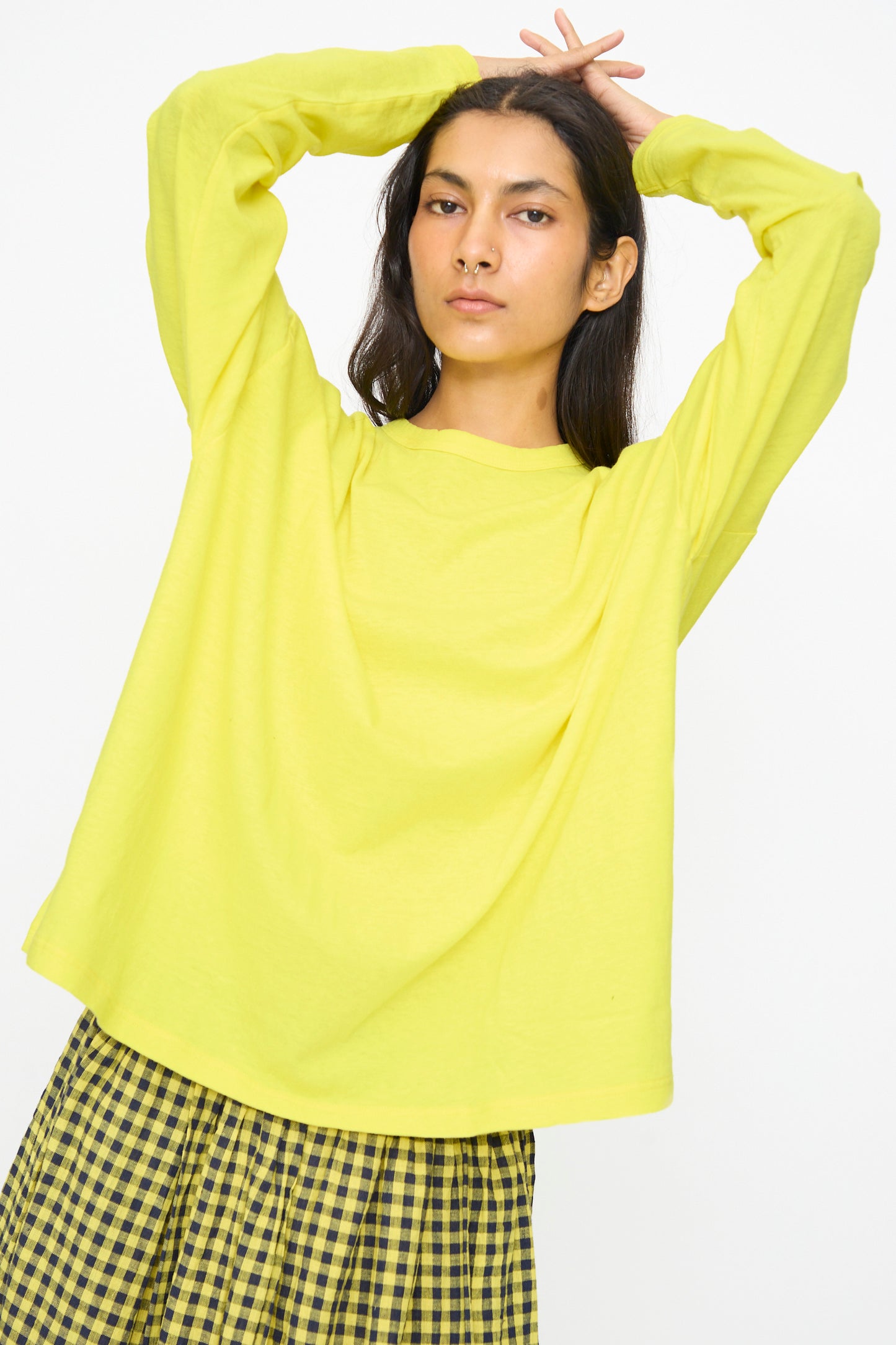 A person wears the Ichi Antiquités Cotton Loose Pullover in Yellow and a yellow plaid skirt, standing with arms raised against a plain white background.