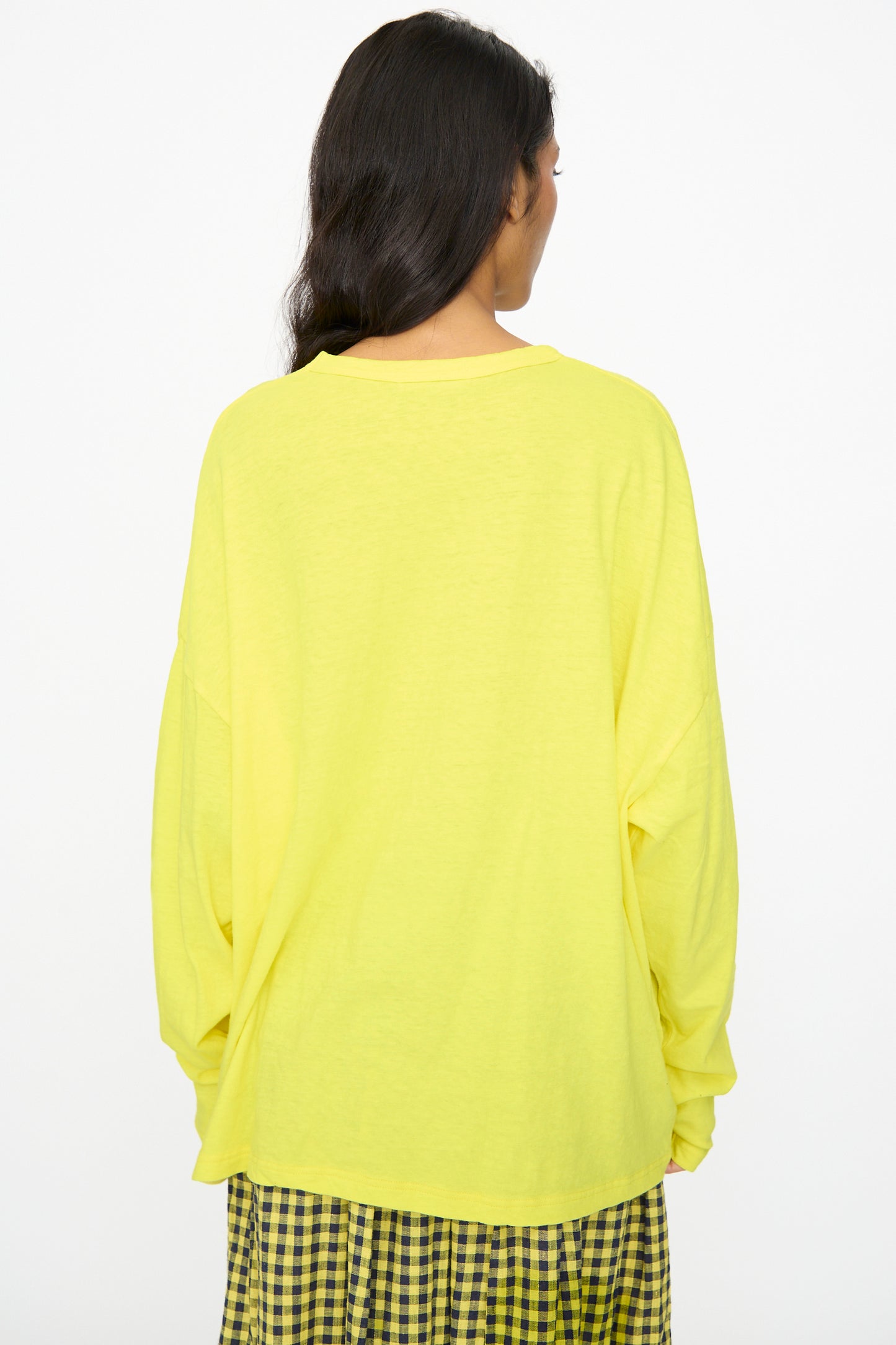 A person stands with their back to the camera, wearing the Ichi Antiquités Cotton Loose Pullover in Yellow paired with a black-and-yellow checkered skirt.