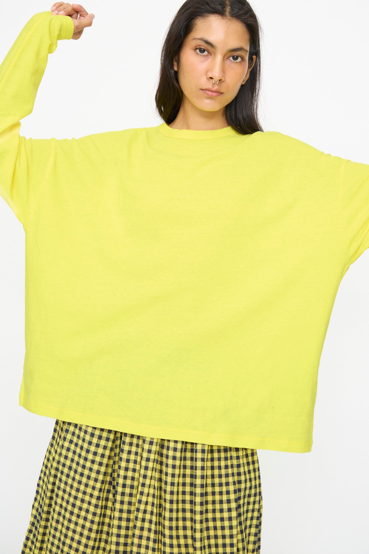 Model wears the Ichi Antiquités Cotton Loose Pullover in Yellow with arms raised, paired with a yellow and black checkered skirt against a plain white background.