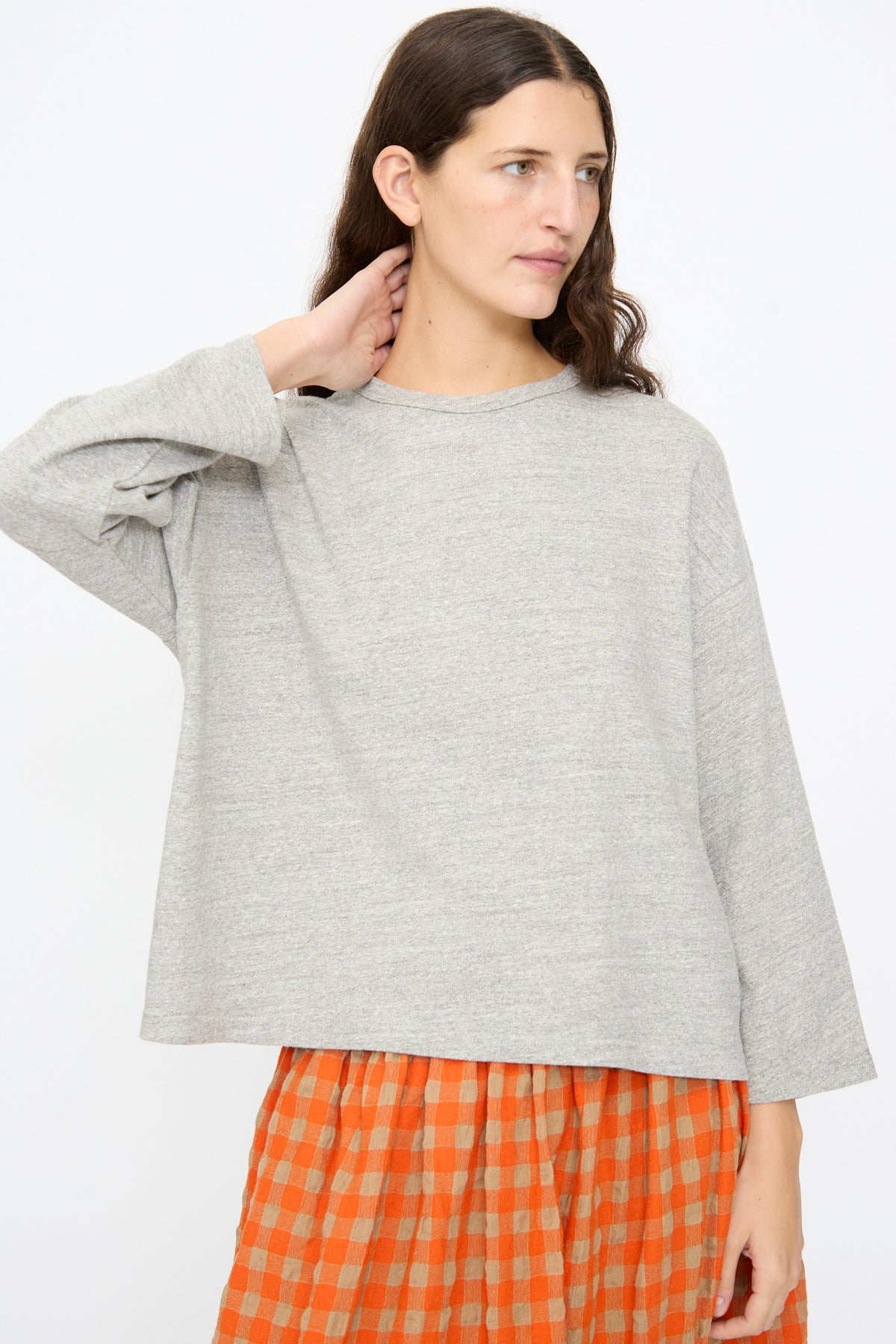 A person wearing an Ichi Antiquités Cotton Pullover in Gray, a relaxed long-sleeved crew-neck top, paired with an orange and beige checkered skirt.