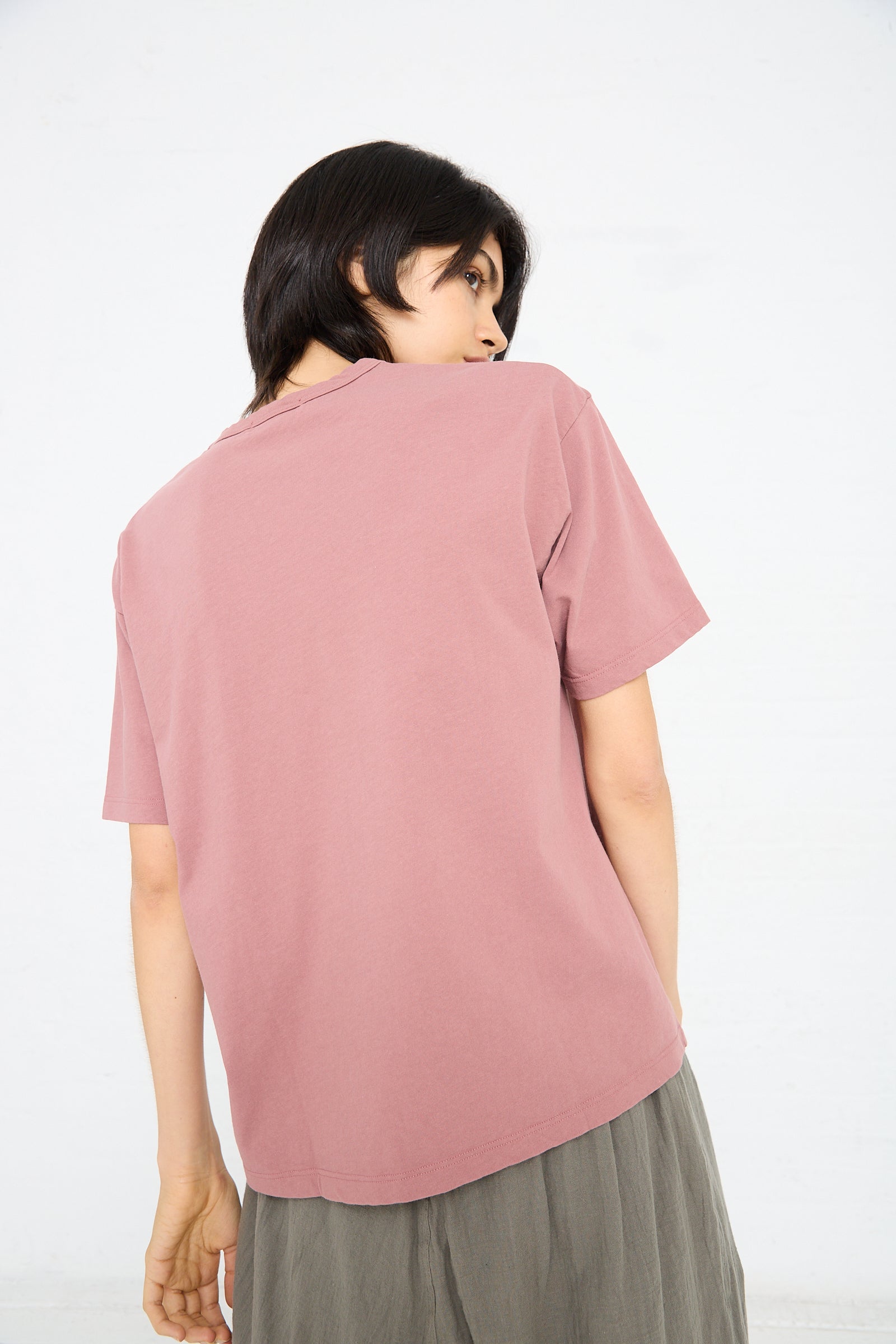 Rear view of a person with dark hair wearing an Ichi Antiquités Cotton Pullover Tee in Pink, looking over their left shoulder. The background is plain white.