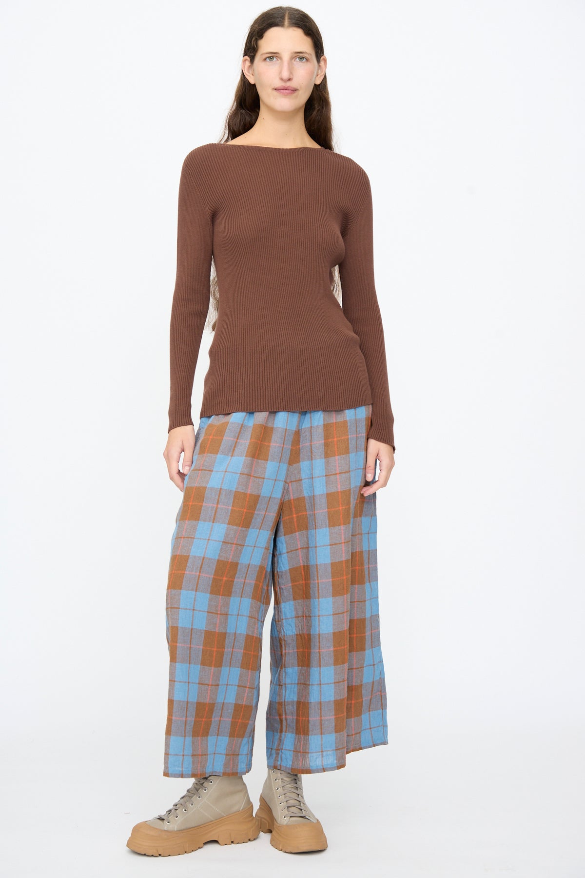 A woman wears an Ichi Antiquités Cotton Rib Knit Pullover in brown, paired with blue and brown plaid wide-leg trousers and tan lace-up sneakers.