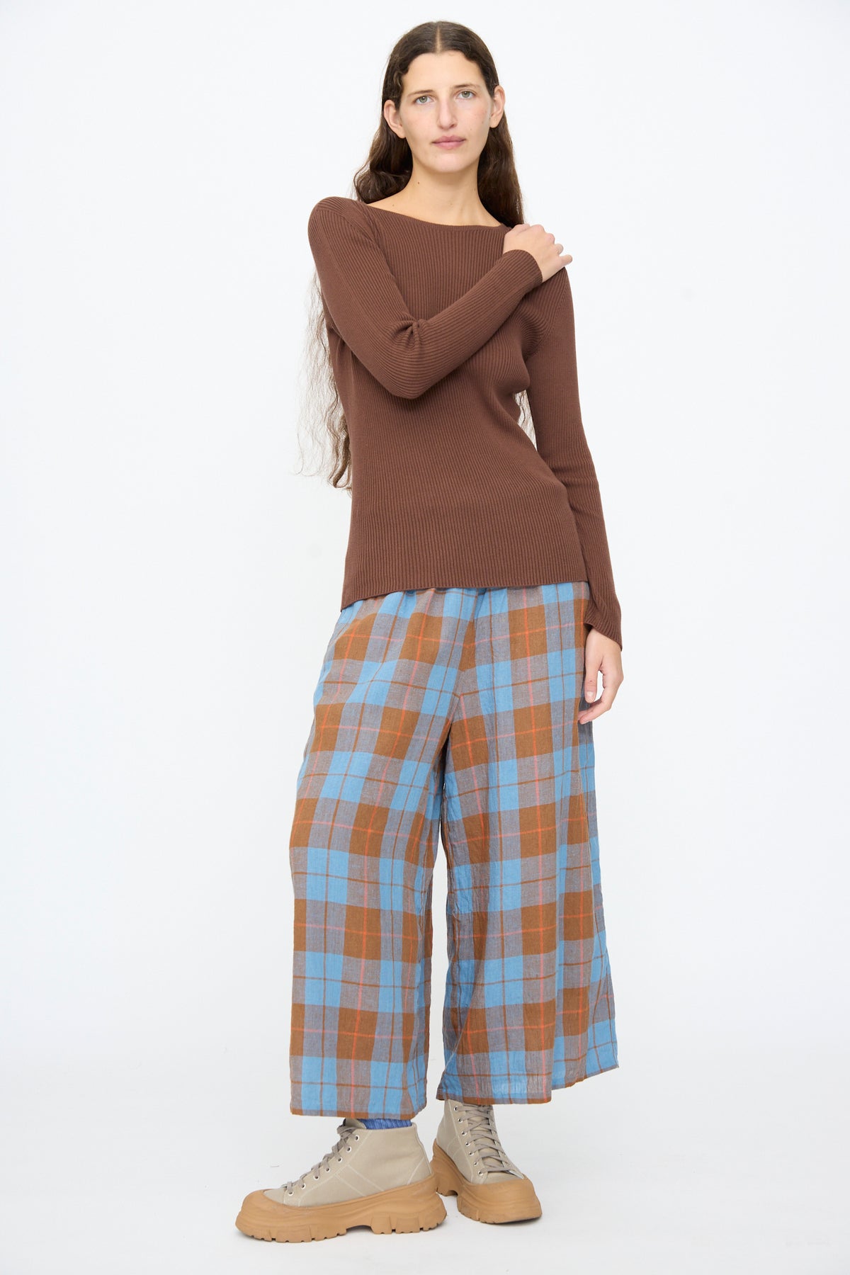 A person wearing a brown Cotton Rib Knit Pullover in Brown by Ichi Antiquités, wide-leg blue and orange plaid pants, and beige lace-up boots.