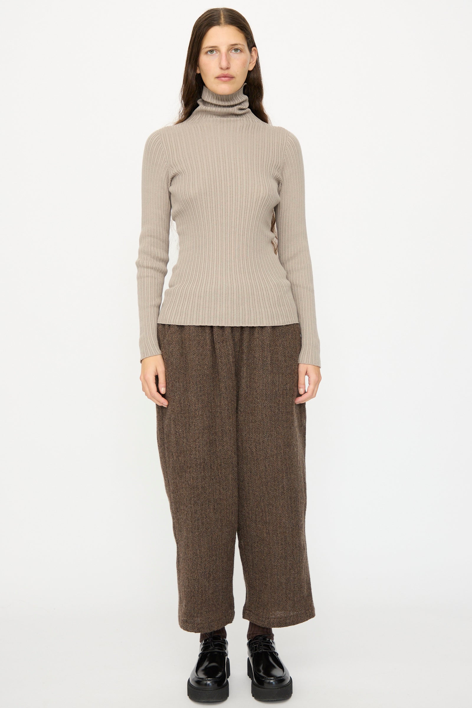 A woman faces forward against a white background, wearing the Ichi Antiquités Cotton Rib Knit Turtleneck in Mocha, loose brown pants, and black shoes.