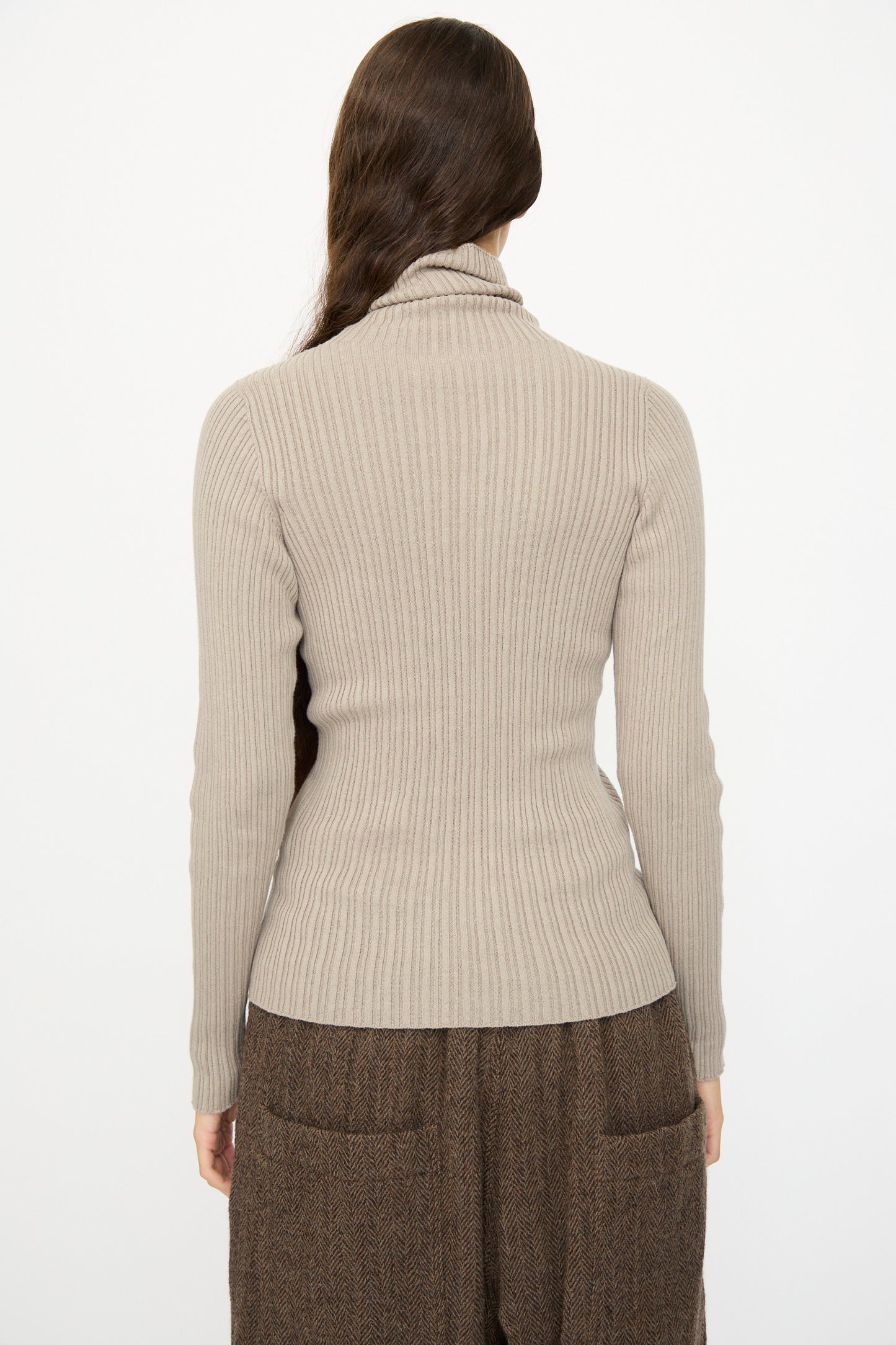 A person with long brown hair is seen from the back wearing the Ichi Antiquités Cotton Rib Knit Turtleneck in Mocha and brown pants, against a plain white background.