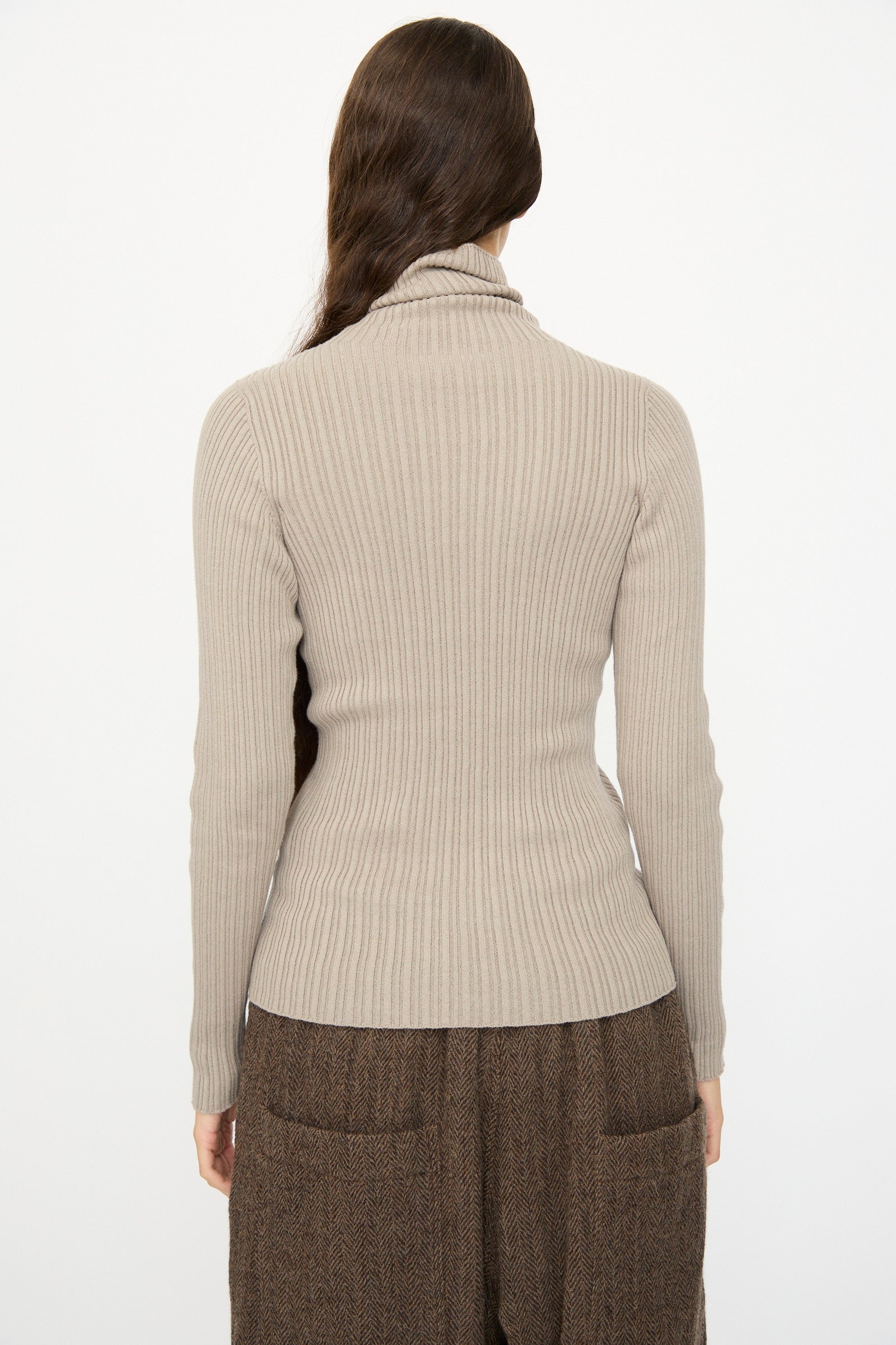 A person with long brown hair is seen from the back wearing the Ichi Antiquités Cotton Rib Knit Turtleneck in Mocha and brown pants, against a plain white background.