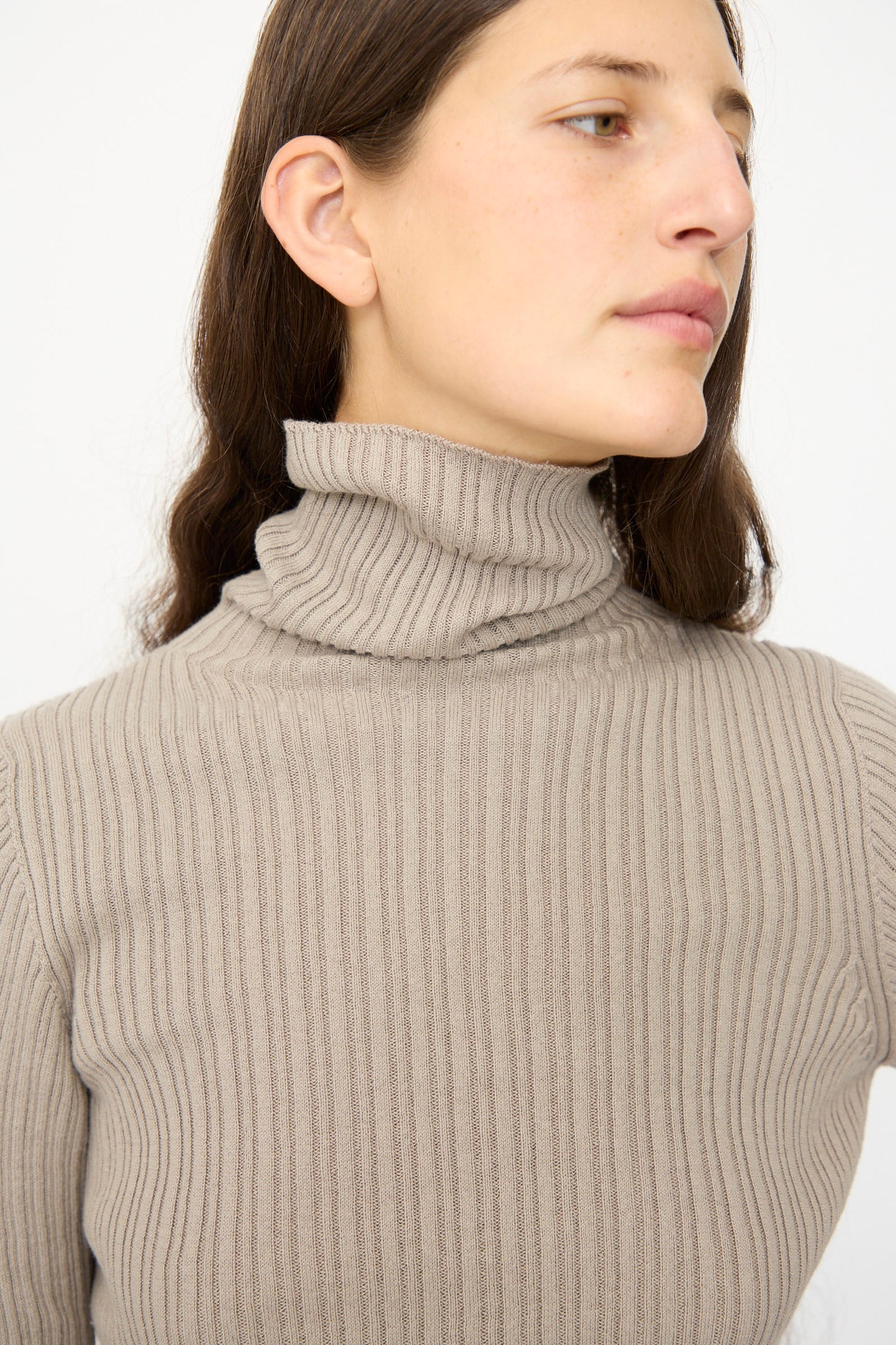 A person with long brown hair wears the Ichi Antiquités Cotton Rib Knit Turtleneck in Mocha, slim fit, facing slightly to the side against a plain background.
