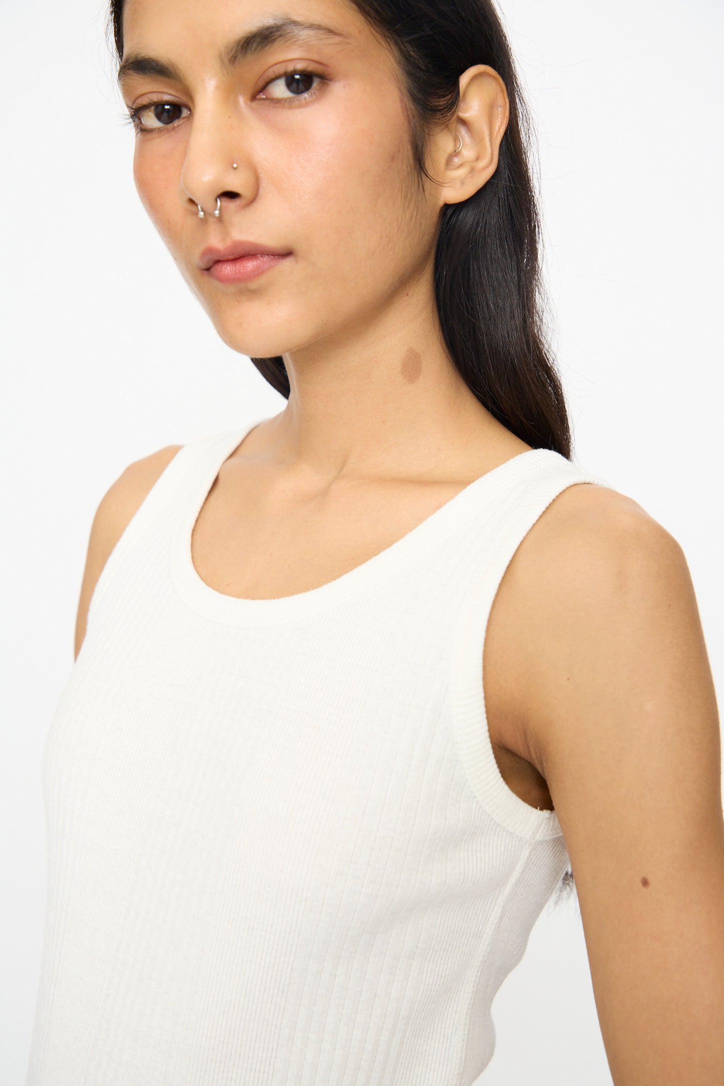 A person with long dark hair wears the Ichi Antiquités Cotton Rib Tank Top in White, featuring a scoop neck, and looks at the camera with a neutral expression.