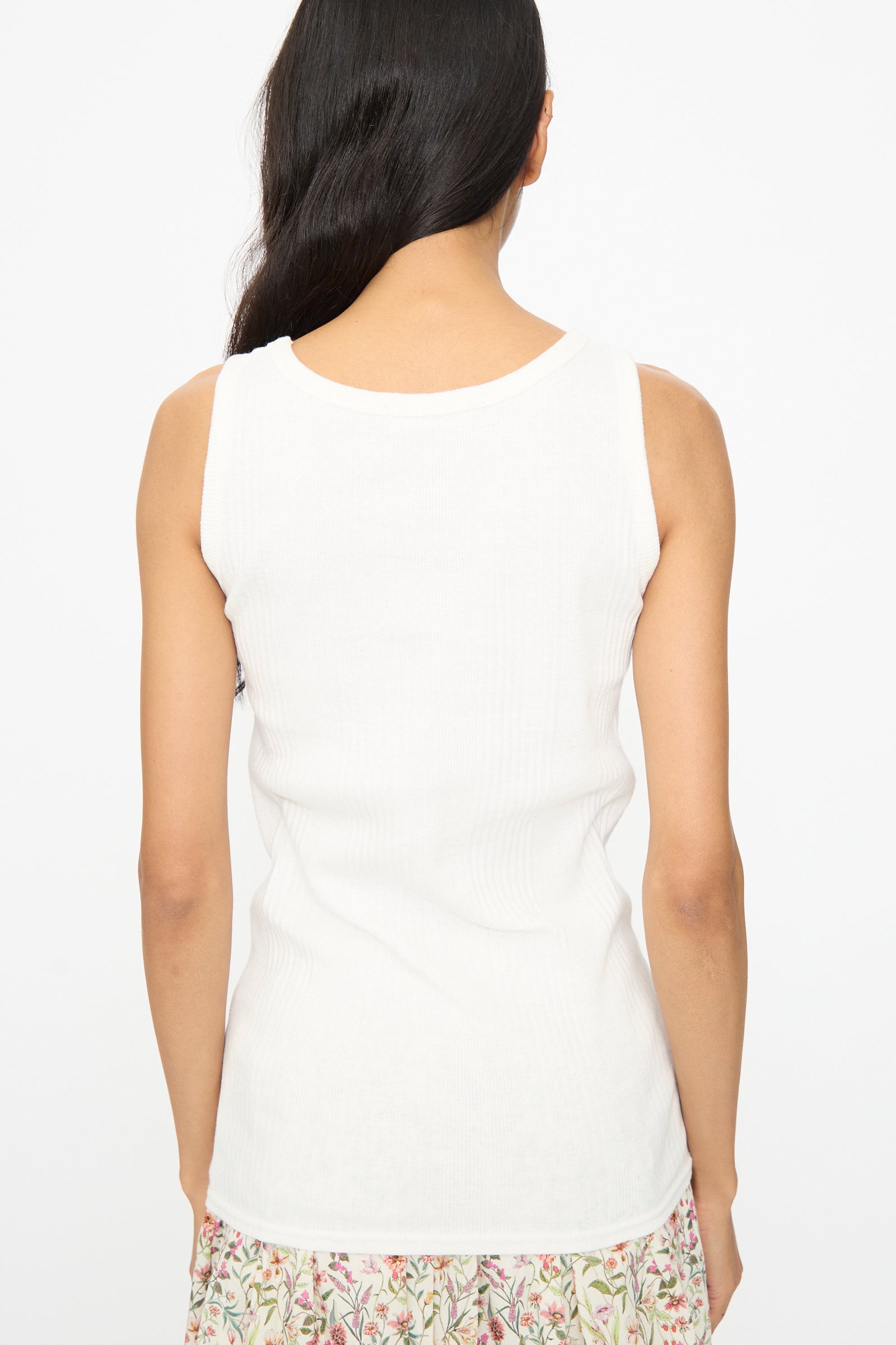 A woman with long dark hair is seen from behind, wearing the Ichi Antiquités Cotton Rib Tank Top in White and a floral skirt against a plain background.