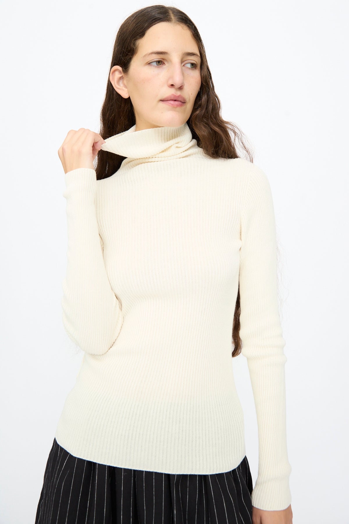 A person wears a slim-fit, ribbed Cotton Rib Turtleneck in Ivory by Ichi Antiquités with black pinstriped trousers.