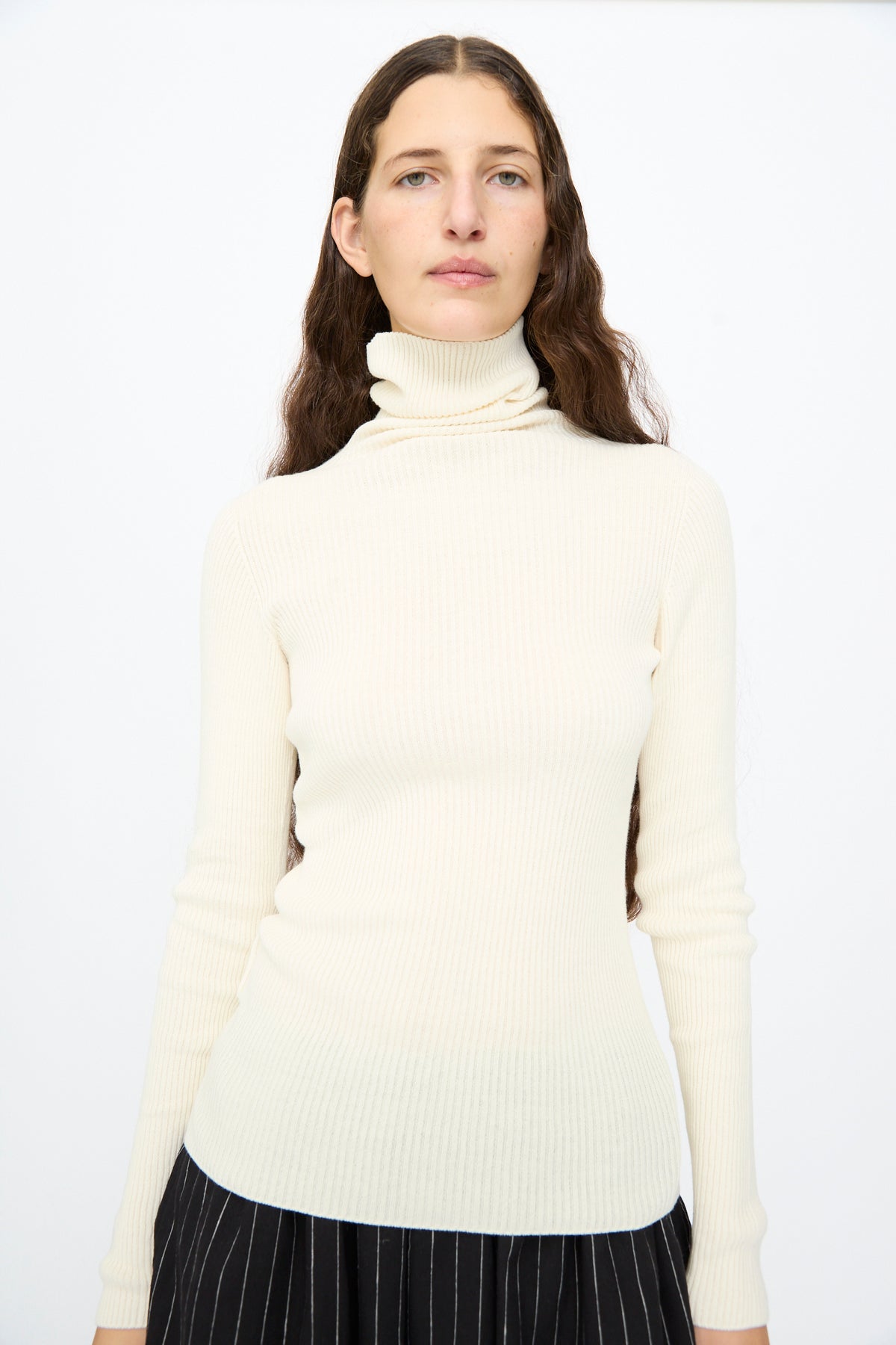 A person wearing an Ichi Antiquités Cotton Rib Turtleneck in Ivory over black pinstriped bottoms.