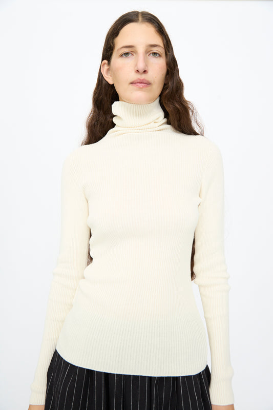 A person wearing an Ichi Antiquités Cotton Rib Turtleneck in Ivory over black pinstriped bottoms.