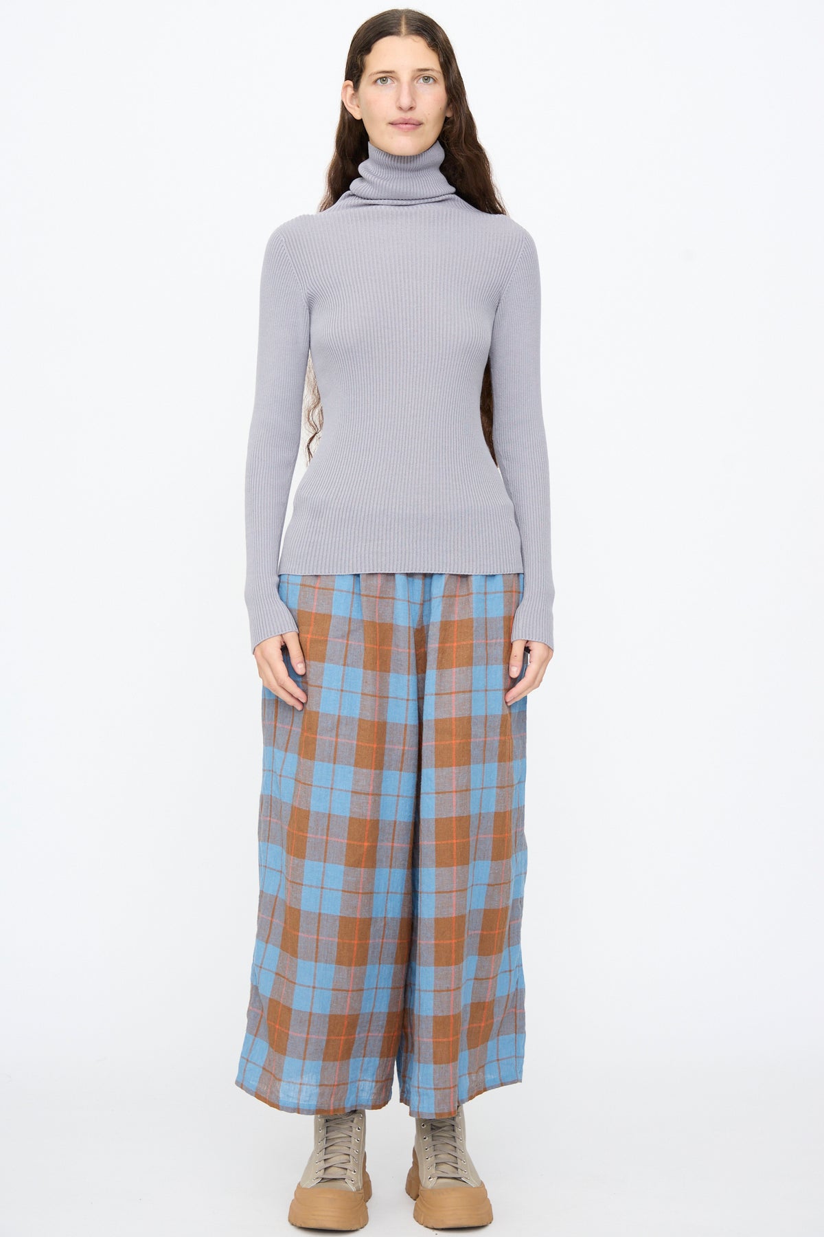A person wearing an Ichi Antiquités Cotton Rib Turtleneck in Light Gray, blue and brown plaid wide-leg trousers, and tan lace-up boots.