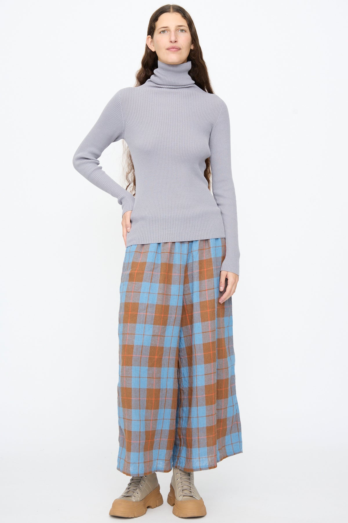 A person wearing an Ichi Antiquités Cotton Rib Turtleneck in Light Gray, loose blue and brown plaid trousers, and tan lace-up shoes.