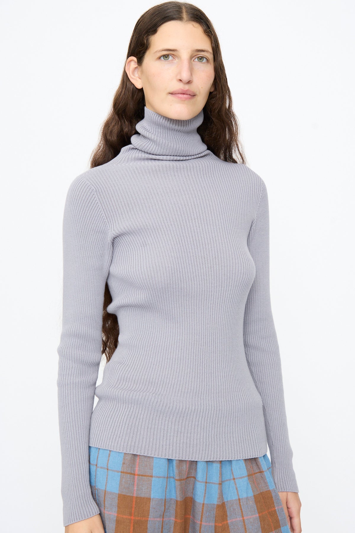 A person wears an Ichi Antiquités Cotton Rib Turtleneck in Light Gray paired with a blue and brown plaid skirt.