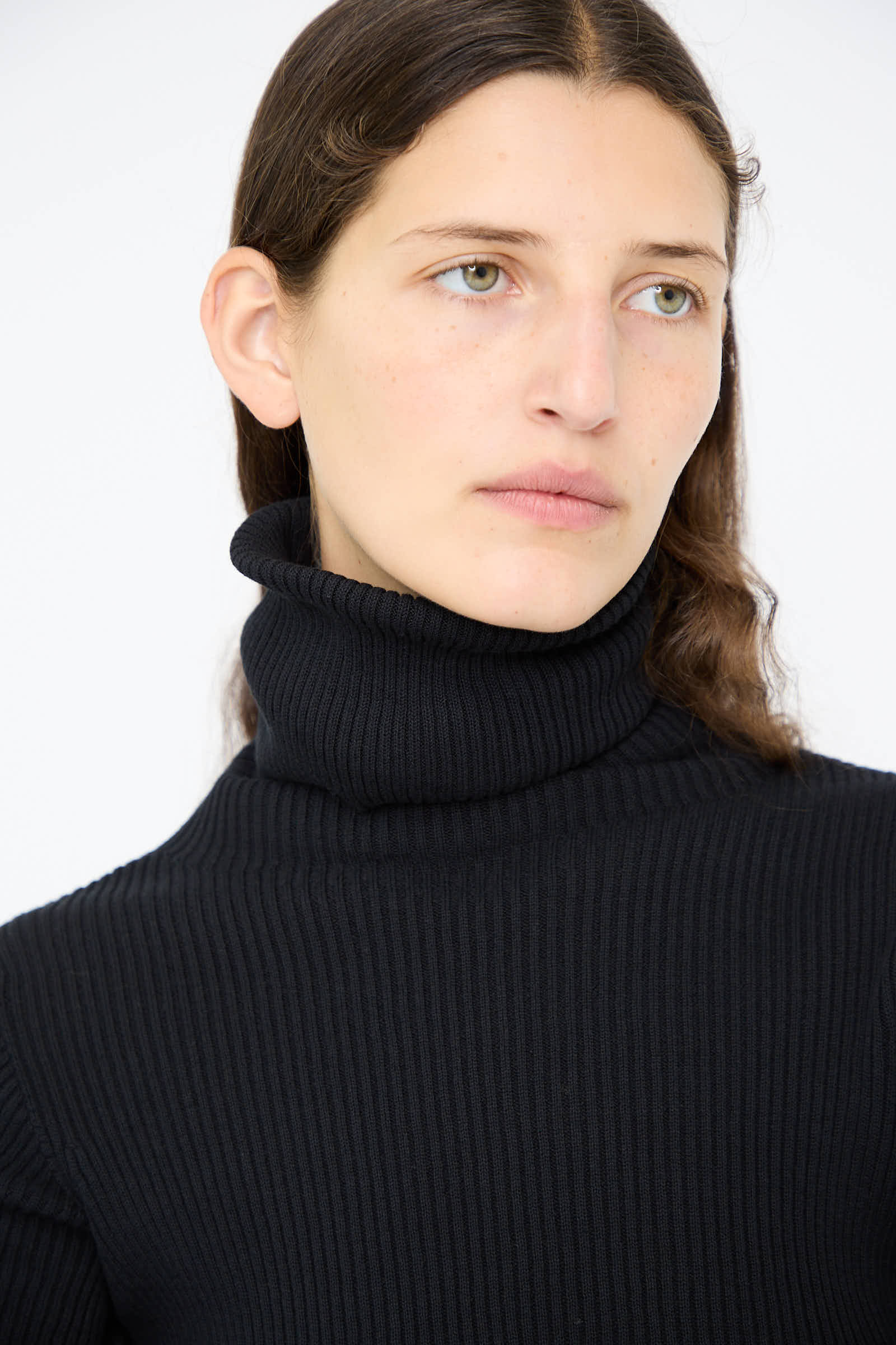 A person with long hair wearing Ichi Antiquités' Cotton Rib Turtleneck in Black, looking to the side against a plain background.