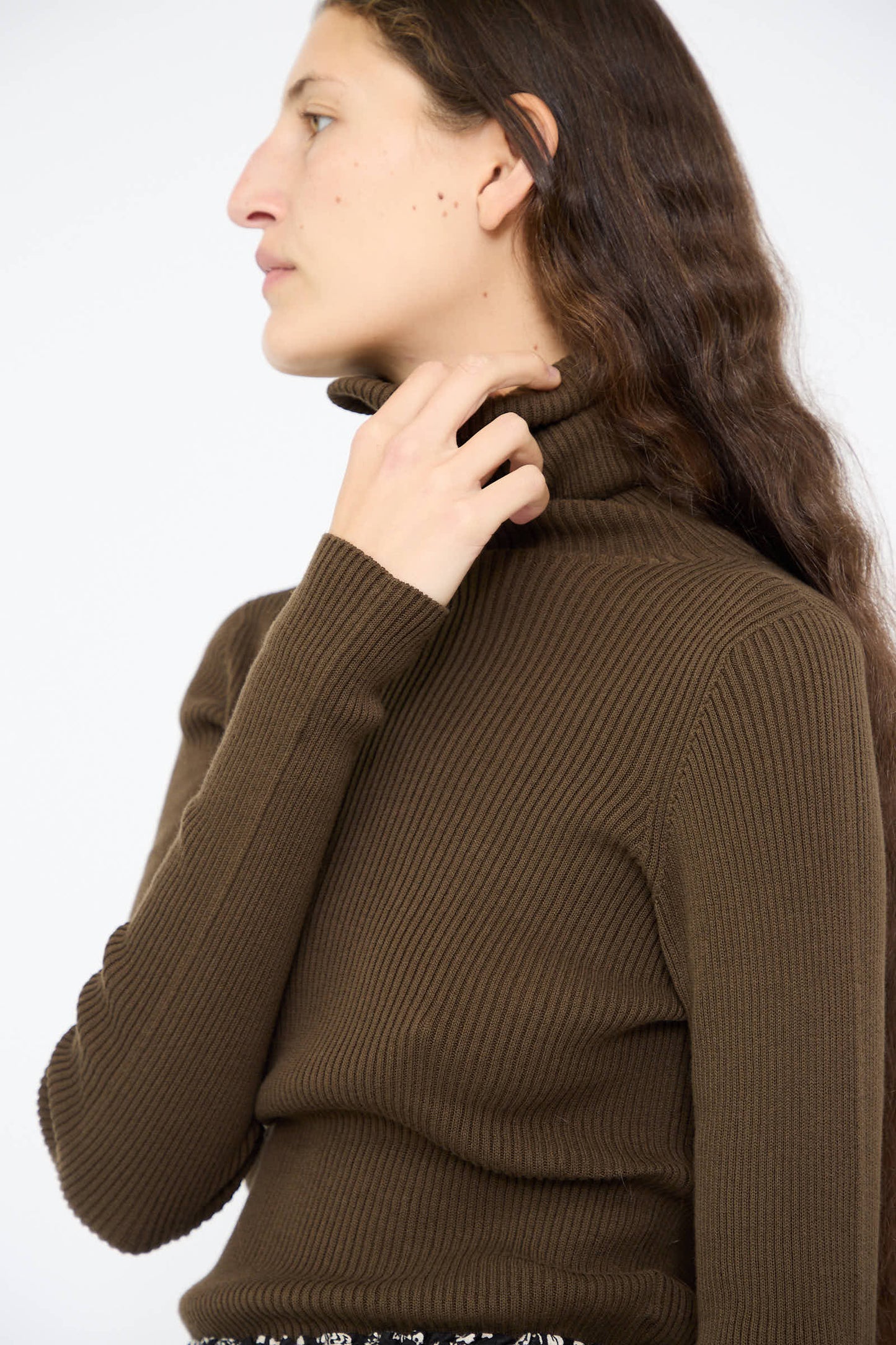 Someone with long hair is wearing the Ichi Antiquités Cotton Rib Turtleneck in brown, looking to the side.