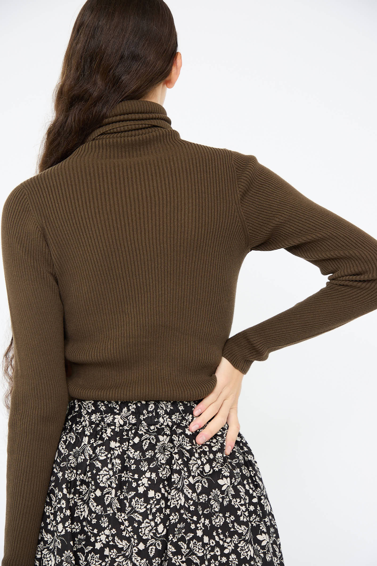 A rear view of someone with long brown hair is shown wearing the Cotton Rib Turtleneck in Brown by Ichi Antiquités, paired with a black and white floral skirt.