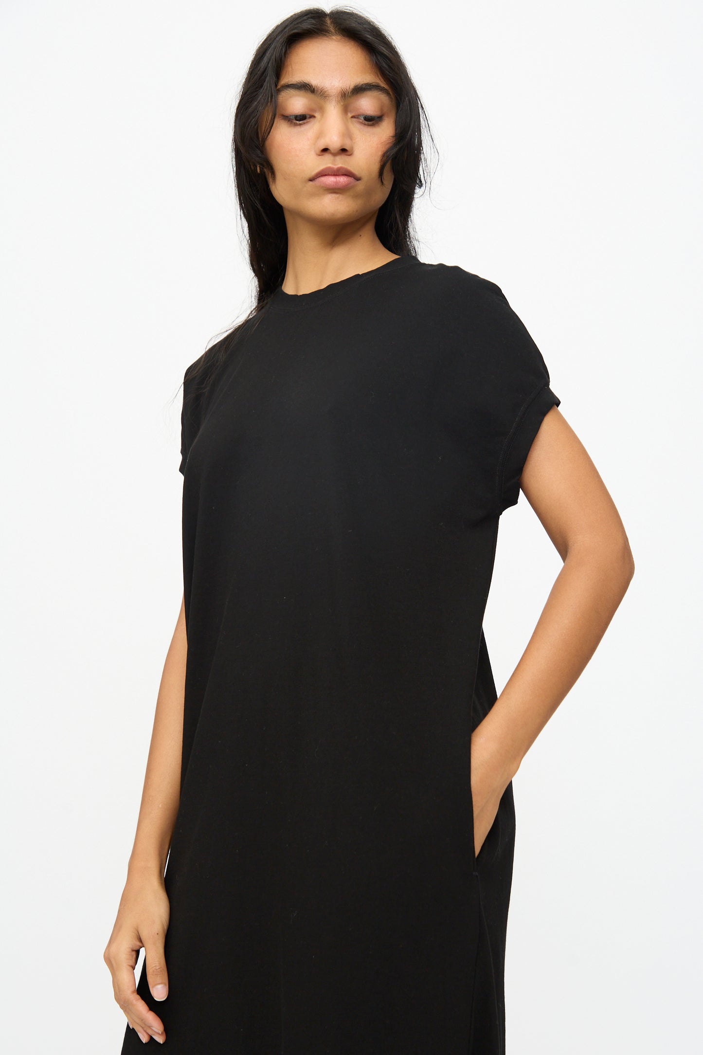 A person models the Ichi Antiquités Cotton Sleeveless Dress in Black, standing against a plain white background with one hand in their pocket.