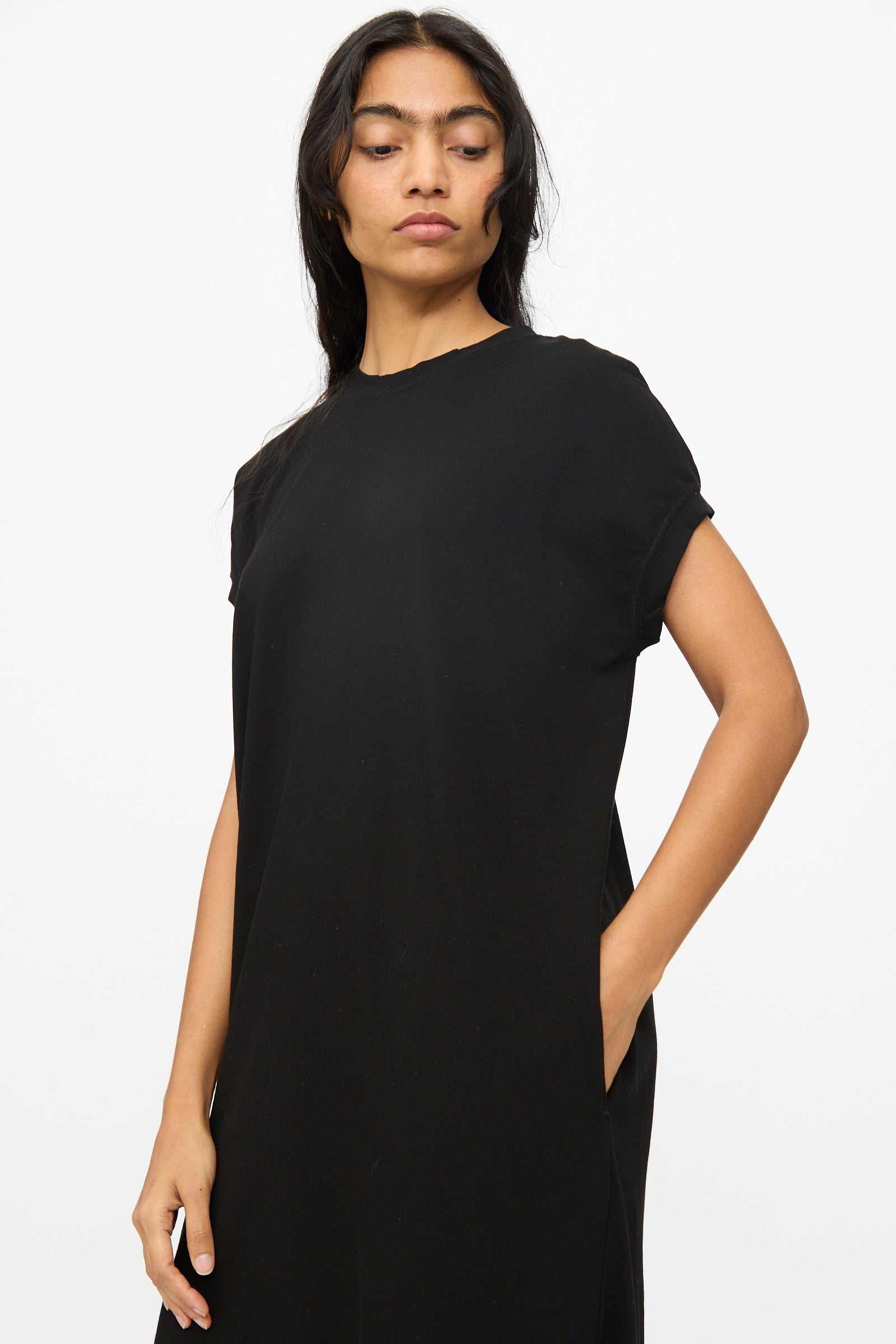 A person models the Ichi Antiquités Cotton Sleeveless Dress in Black, standing against a plain white background with one hand in their pocket.