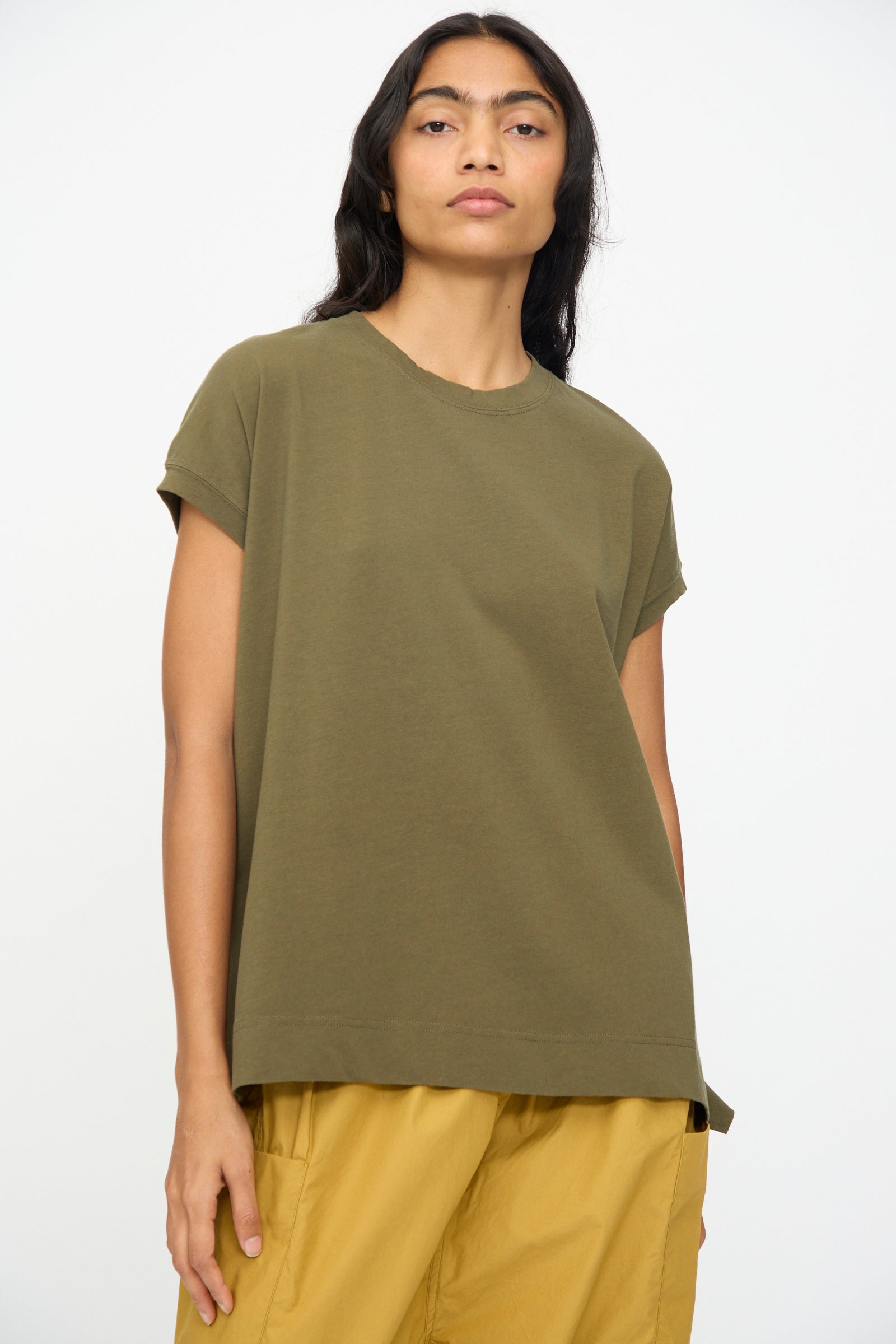 A person wears the Ichi Antiquités Cotton Sleeveless Tee in Khaki paired with mustard yellow pants, standing against a plain light background.
