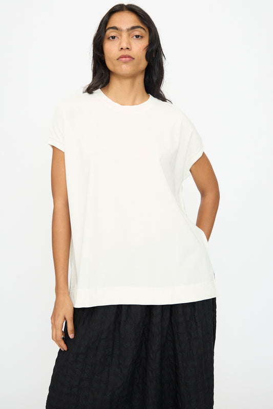 A person stands against a plain background, wearing the Ichi Antiquités Cotton Sleeveless Tee in White paired with a black textured skirt.
