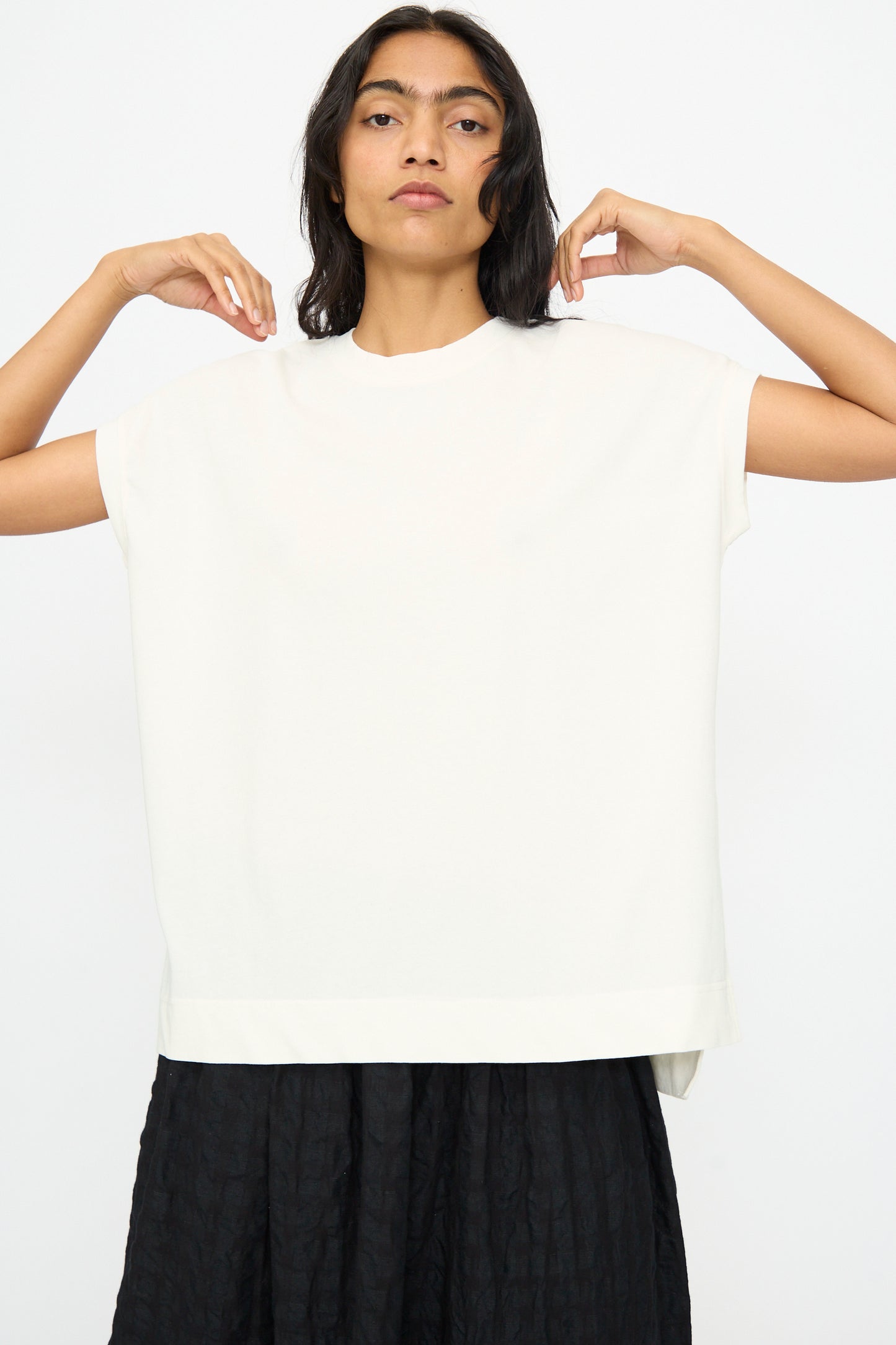 A person wears the Ichi Antiquités Cotton Sleeveless Tee in White and a black textured skirt, standing against a plain white background with arms slightly raised.